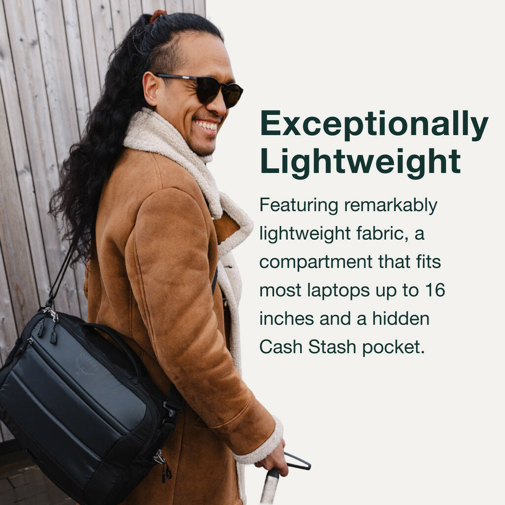 Person holding a black Osprey Ozone travel bag, wearing a brown coat.