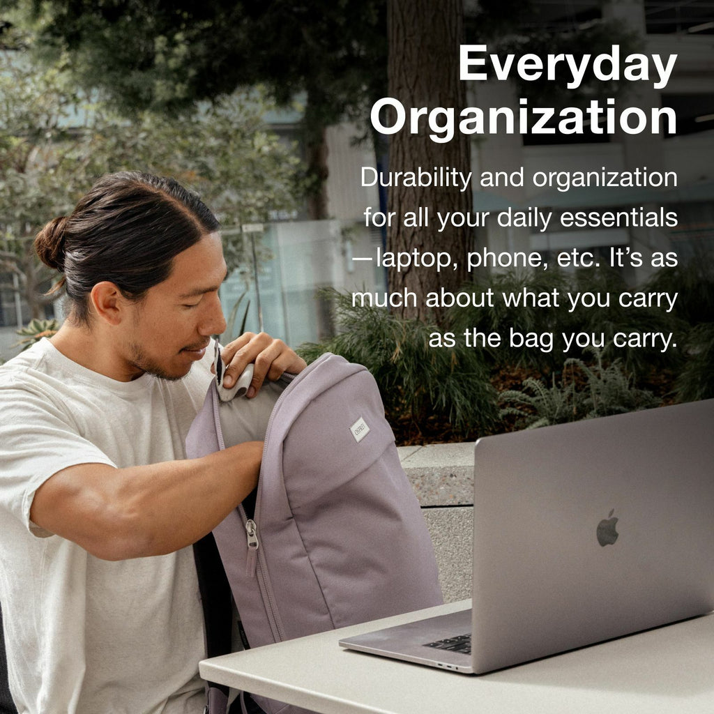 A man sits at an outdoor table with an open laptop, reaching into a lavender backpack. Text about everyday organization appears beside him.