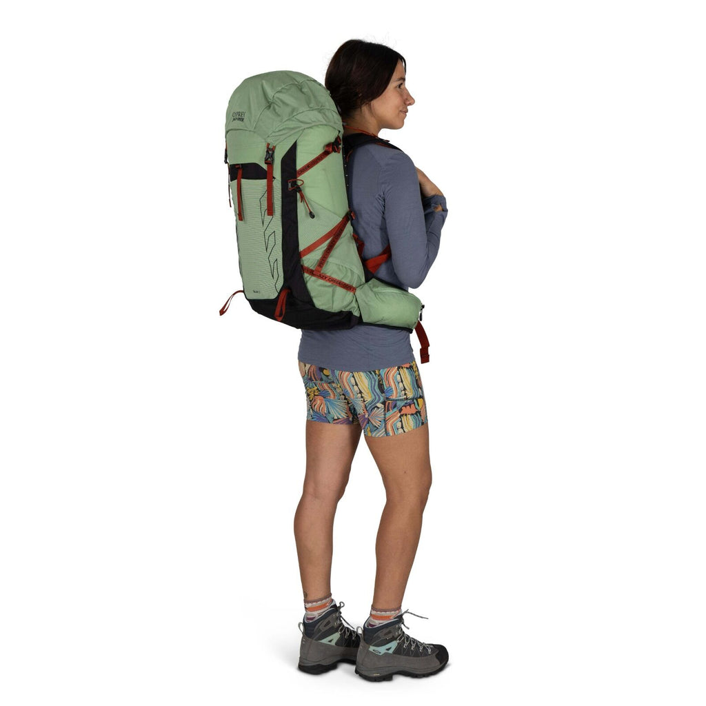 A hiker in colorful shorts and a long-sleeve shirt carries a large green backpack, ready for an outdoor adventure.