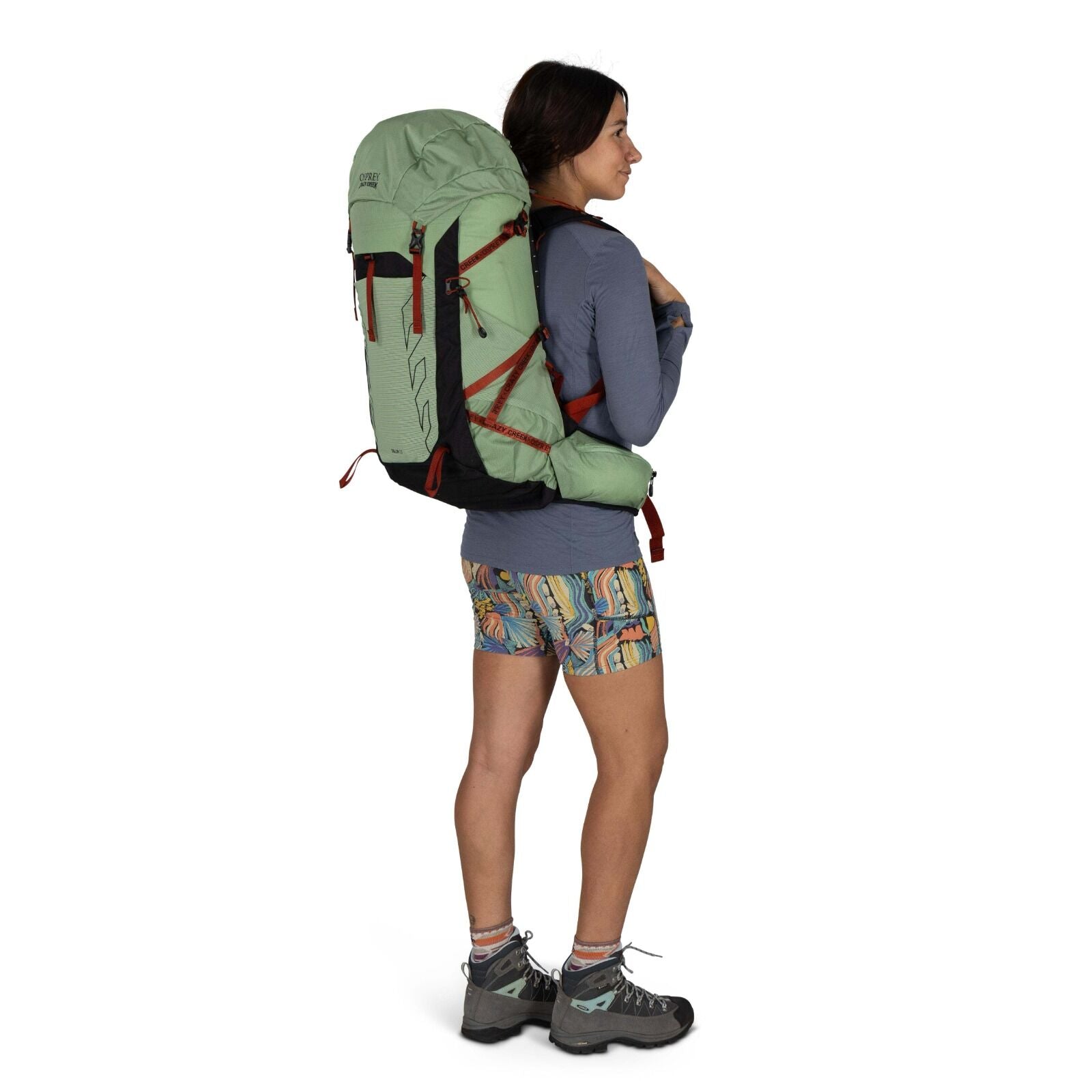 A hiker in colorful shorts and a long-sleeve shirt carries a large green backpack, ready for an outdoor adventure.