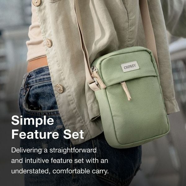 A person wearing a beige jacket carries a small green Osprey crossbody bag, showcasing its simple and comfortable design.