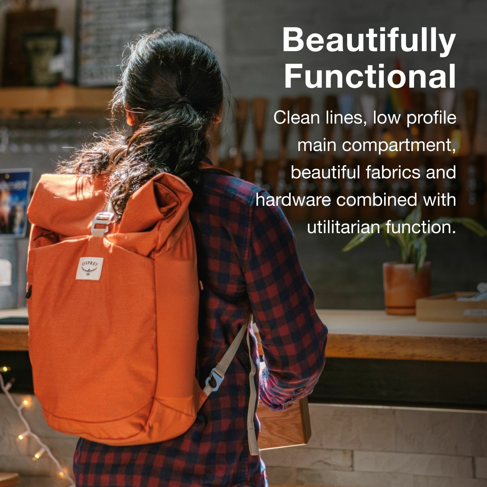 A person in a checkered shirt carries a stylish orange Osprey backpack with clean lines and functional design, set against a cozy café backdrop.