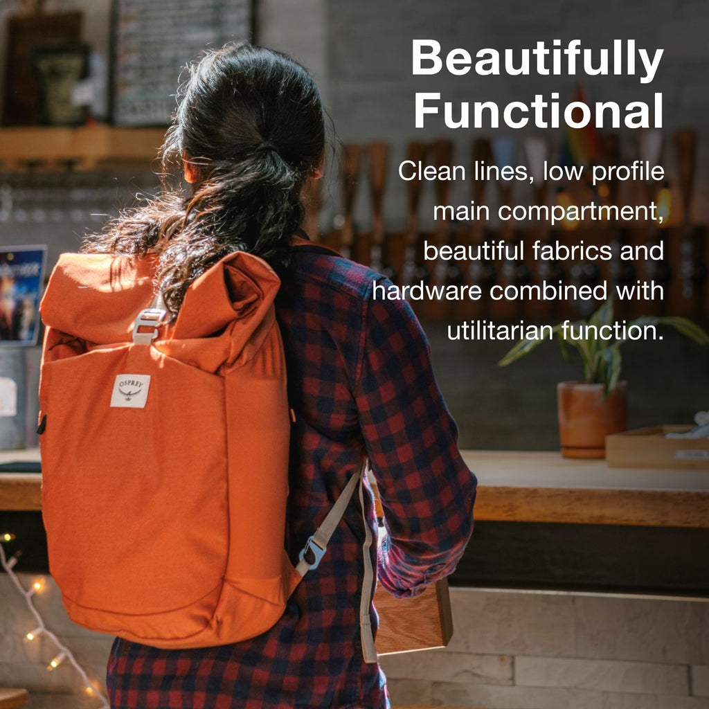 A person in a checkered shirt carries a stylish orange Osprey backpack with clean lines and functional design, set against a cozy café backdrop.
