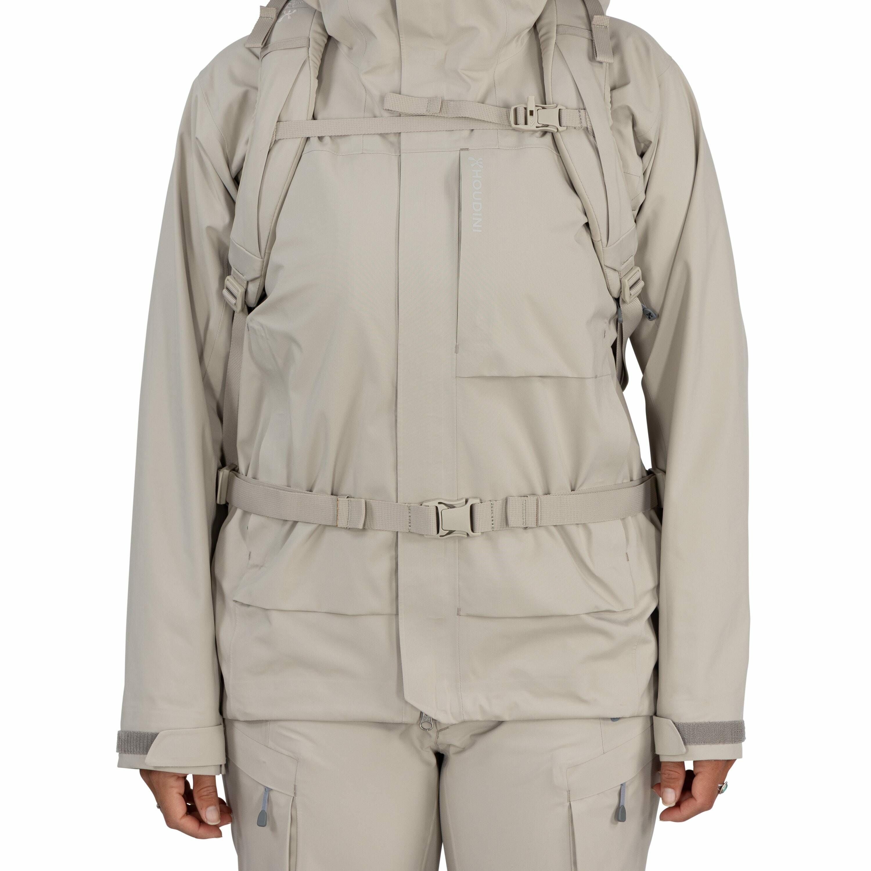 The image shows a person wearing a light gray outdoor jacket and pants set, likely designed for cold or wet weather. The jacket is equipped with several features for practicality and comfort: it has a high collar for warmth, a front zipper concealed by a