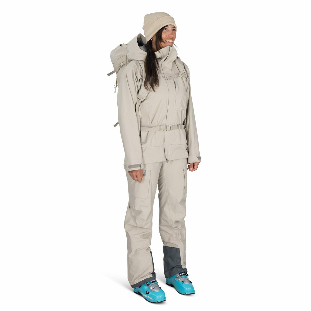The image shows a person dressed in light gray outdoor gear, likely designed for cold weather activities such as hiking or skiing. They are wearing a matching jacket and pants set, both of which appear to be insulated and weatherproof, suggesting they are