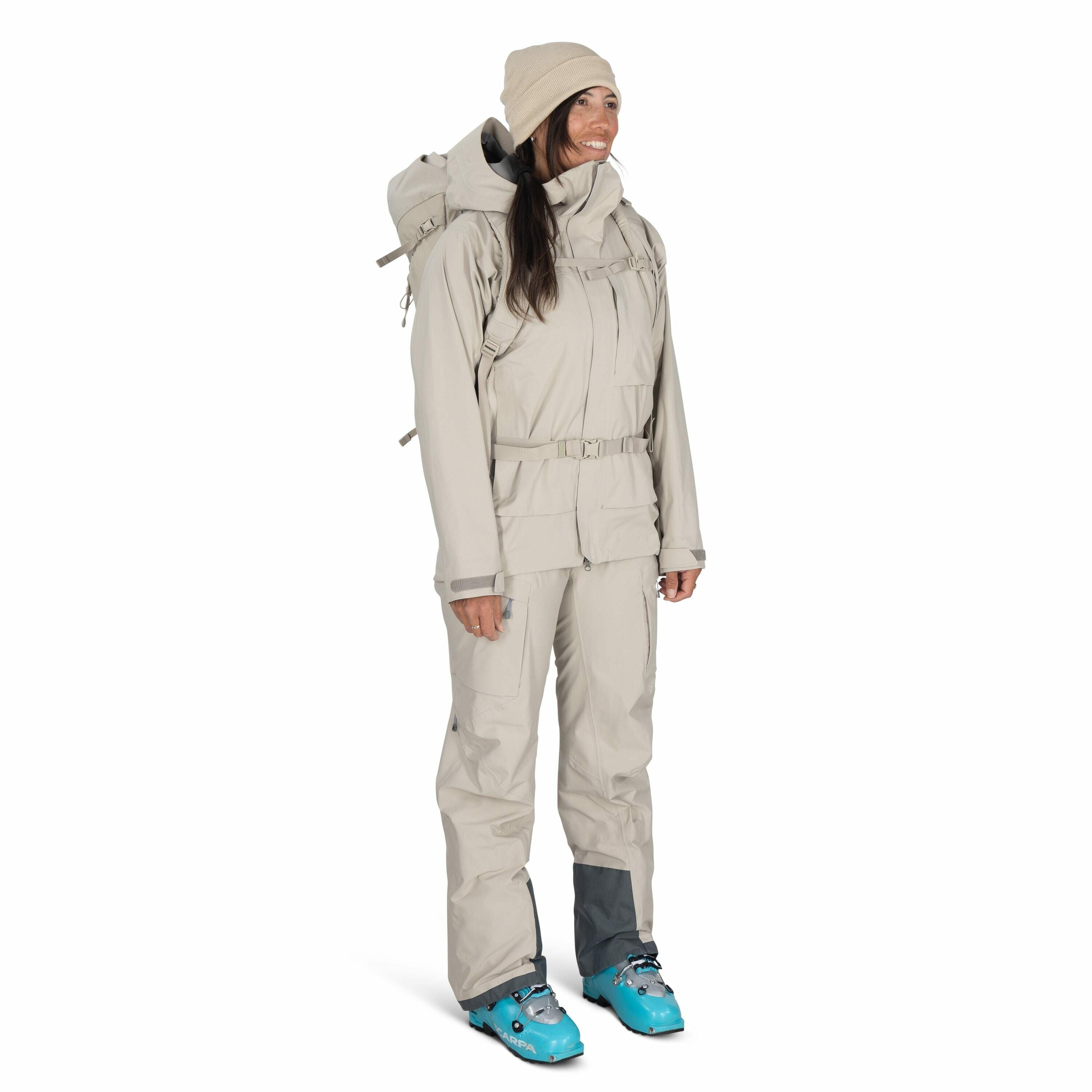The image shows a person dressed in light gray outdoor gear, likely designed for cold weather activities such as hiking or skiing. They are wearing a matching jacket and pants set, both of which appear to be insulated and weatherproof, suggesting they are