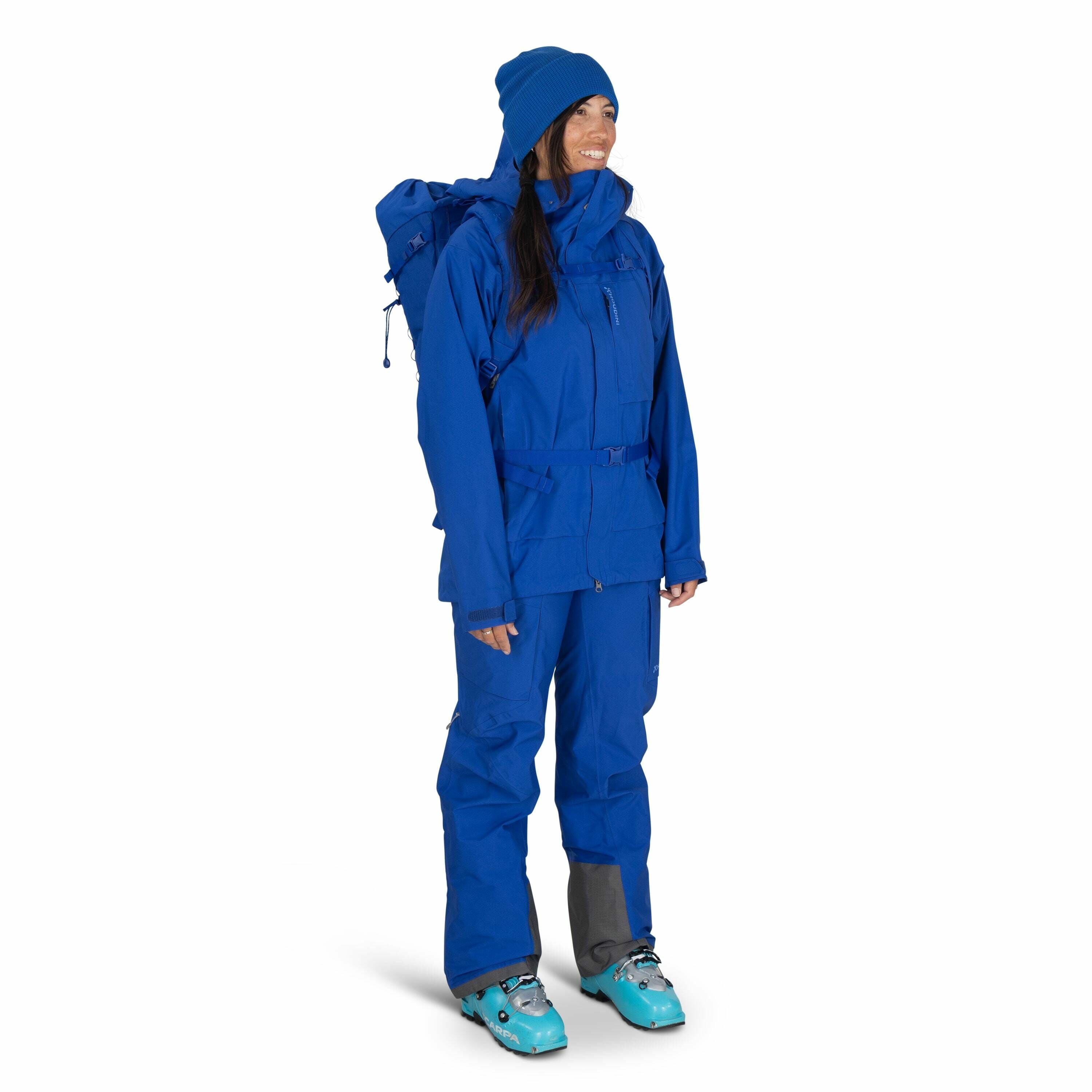 The image depicts a person dressed in a complete set of blue outdoor gear, likely designed for cold-weather activities such as skiing or snowboarding. They are wearing a blue jacket with a hood and matching pants, which appear to be waterproof and insulat
