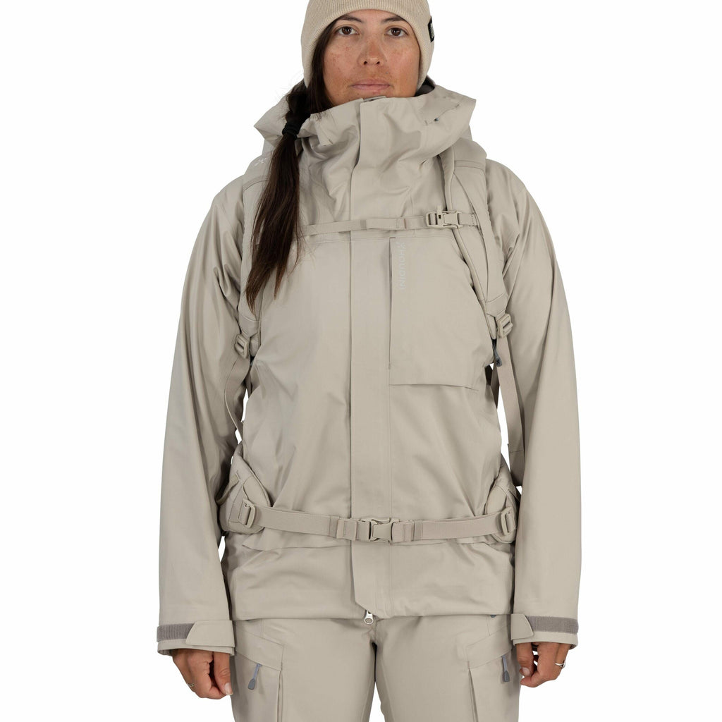 The image depicts a person wearing a light beige, technical outerwear ensemble suitable for cold or wet weather conditions. The outfit consists of a hooded jacket and matching pants, made from what appears to be water-resistant material. The jacket featur