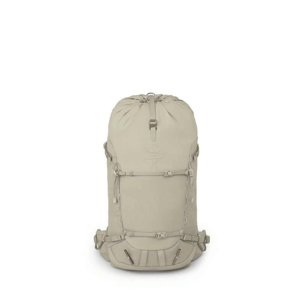 The image shows a light beige backpack with a minimalist and functional design. It features a drawstring closure at the top and a flap that likely secures with a clip. The front of the backpack has a series of loops for attaching gear, as well as two hori