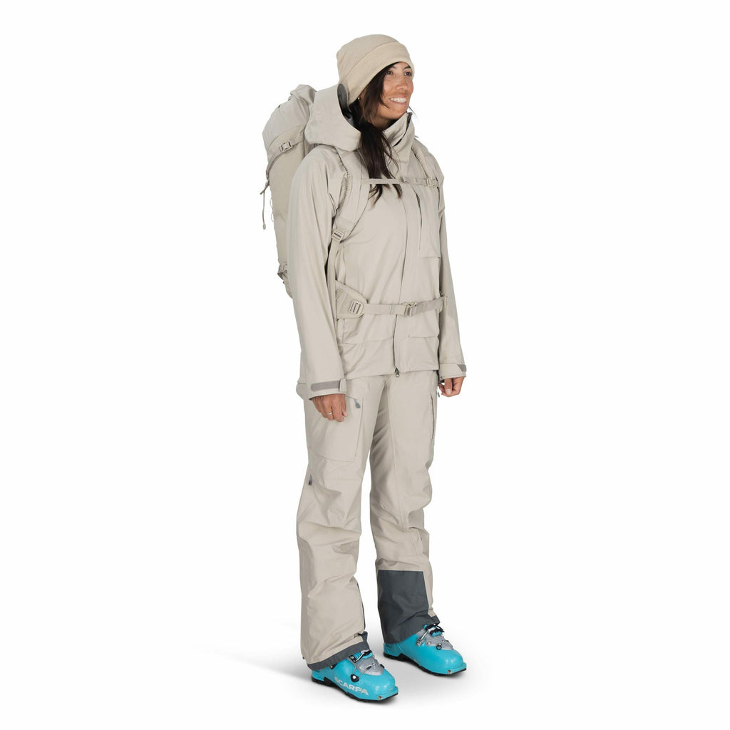 The image shows a person dressed in beige outdoor attire, suitable for cold or mountainous environments. They are wearing a full beige outfit, consisting of a jacket with multiple pockets and matching pants, providing ample protection against the elements