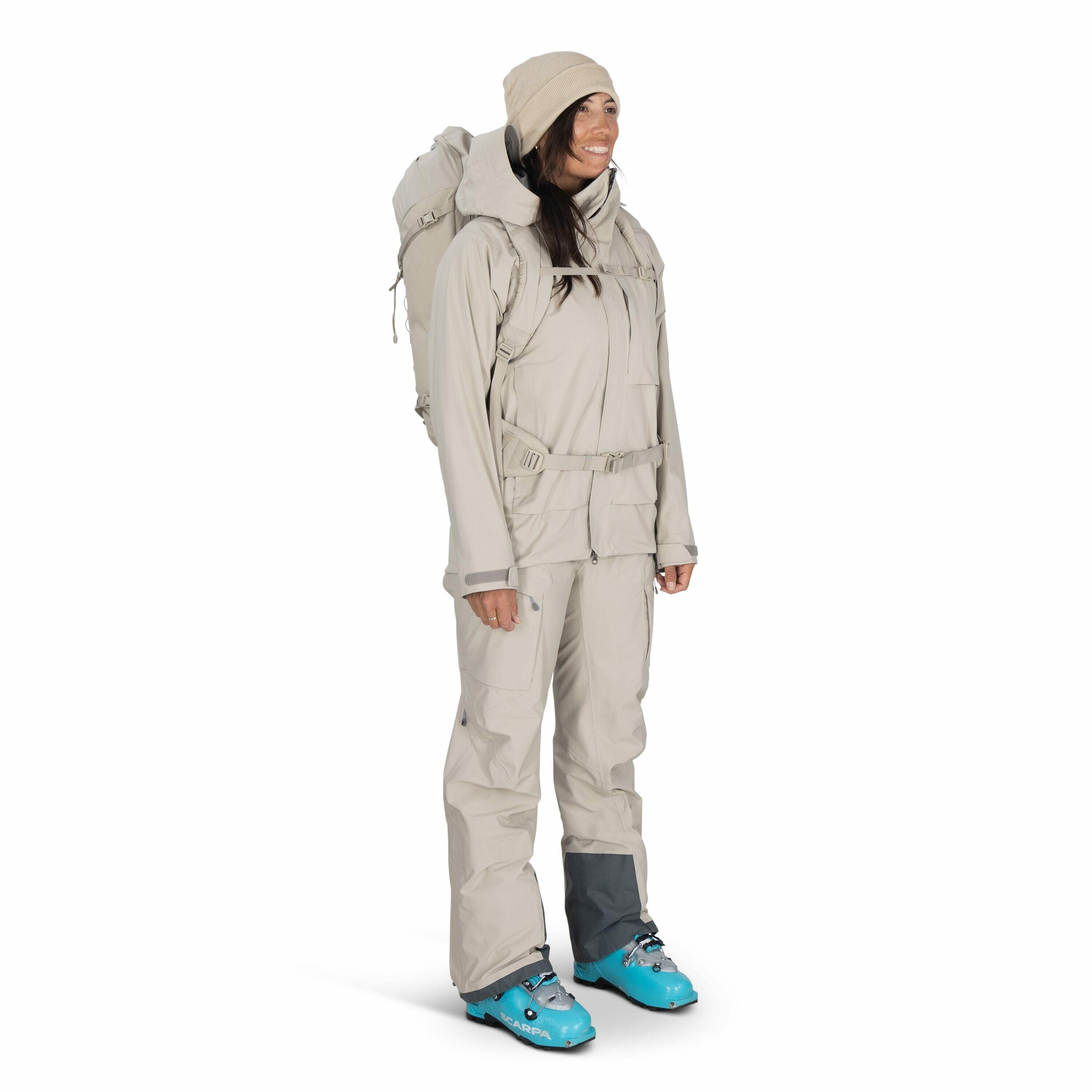 The image shows a person dressed in beige outdoor attire, suitable for cold or mountainous environments. They are wearing a full beige outfit, consisting of a jacket with multiple pockets and matching pants, providing ample protection against the elements