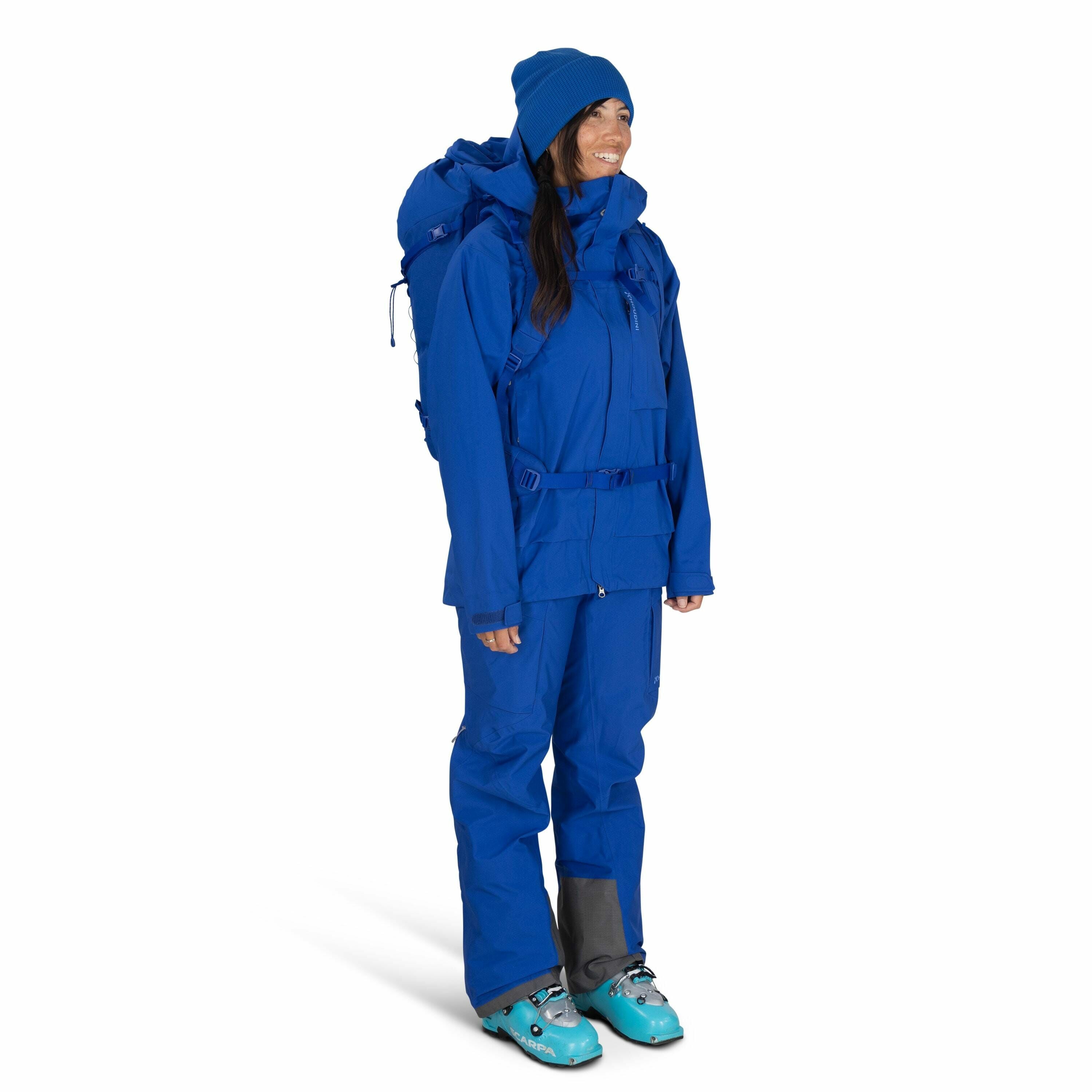 The image shows a person wearing a complete set of blue outdoor gear suitable for cold weather or mountain activities. The attire includes a blue jacket with multiple pockets and adjustable straps, matching blue pants, and a blue backpack. Additionally, t