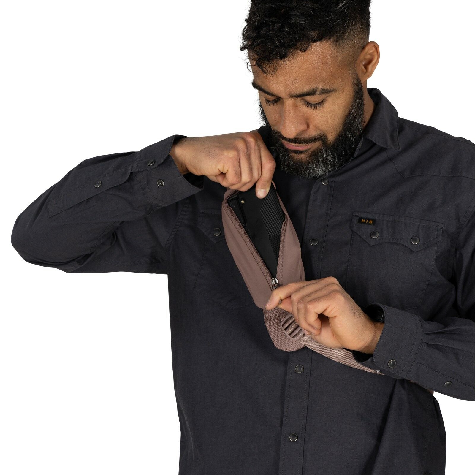 The image features a man wearing a dark gray button-up shirt, placing or retrieving a pair of sunglasses with orange lenses from a small, front pocket of a taupe-colored backpack. The backpack has a black patch with the Osprey logo prominently displayed o