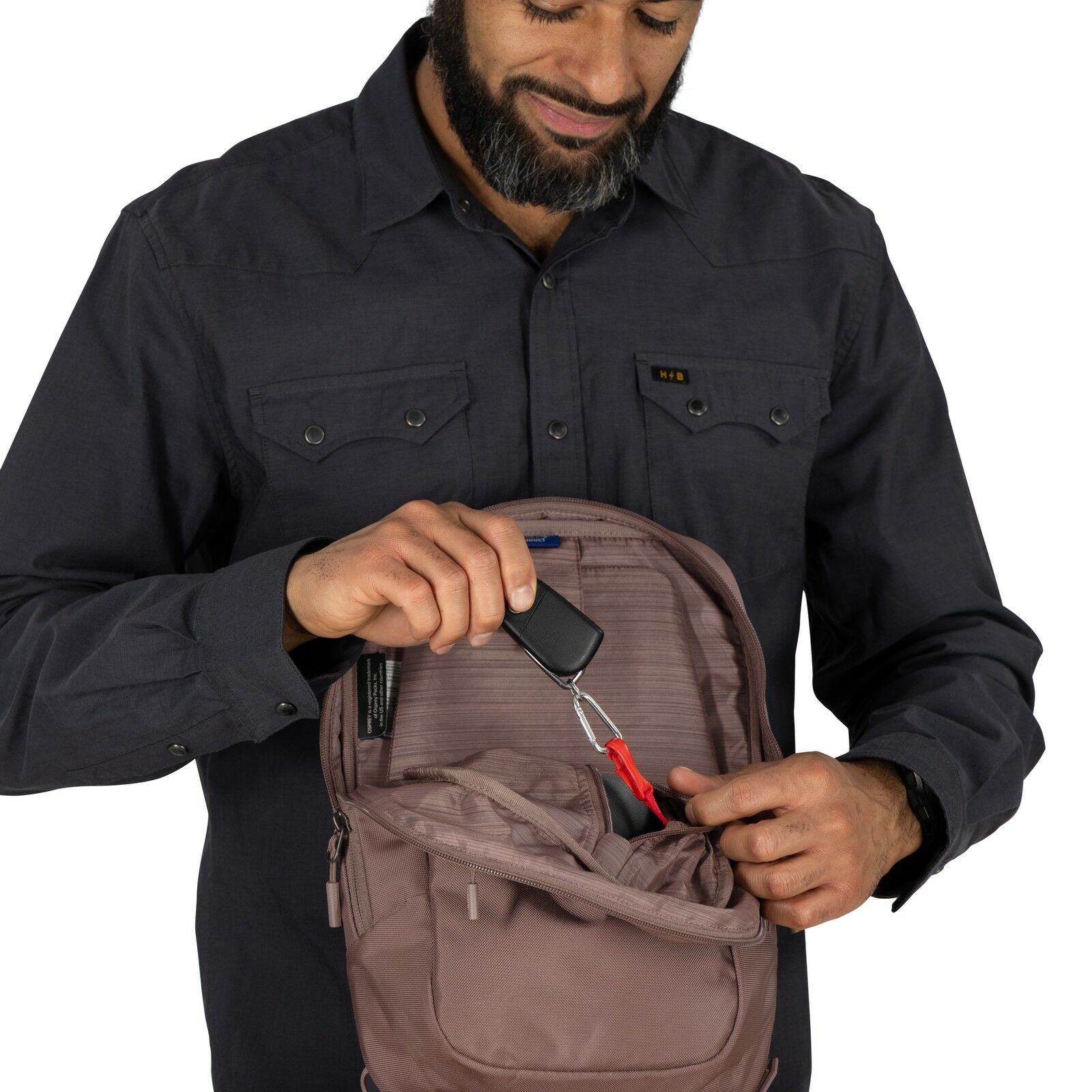 The image shows a person dressed in a long-sleeved, dark-colored button-up shirt. The individual is holding a small, brown pouch or bag close to their chest, which appears to be secured around the neck with a strap. Inside the pouch, a smartphone is parti