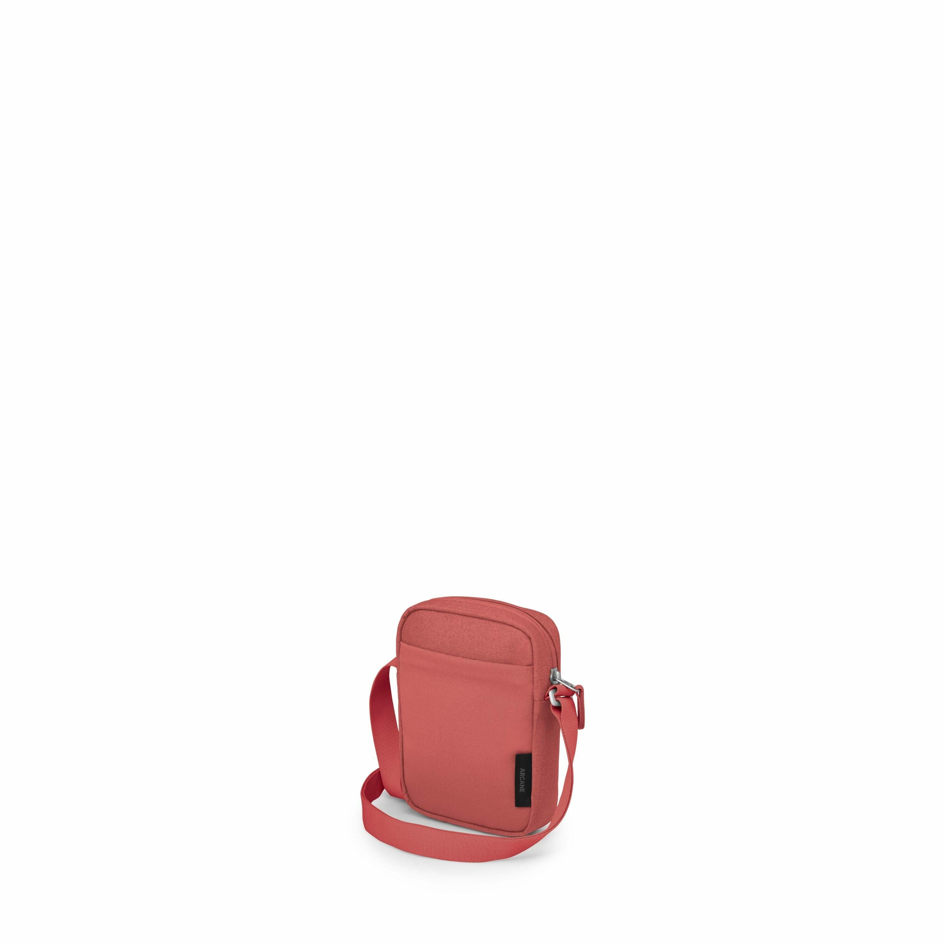 The image displays a small, red crossbody bag with a minimalist design. The bag has a front pocket with a zipper closure and a main compartment that appears to also have a zip closure. It features an adjustable shoulder strap for convenient carrying. The