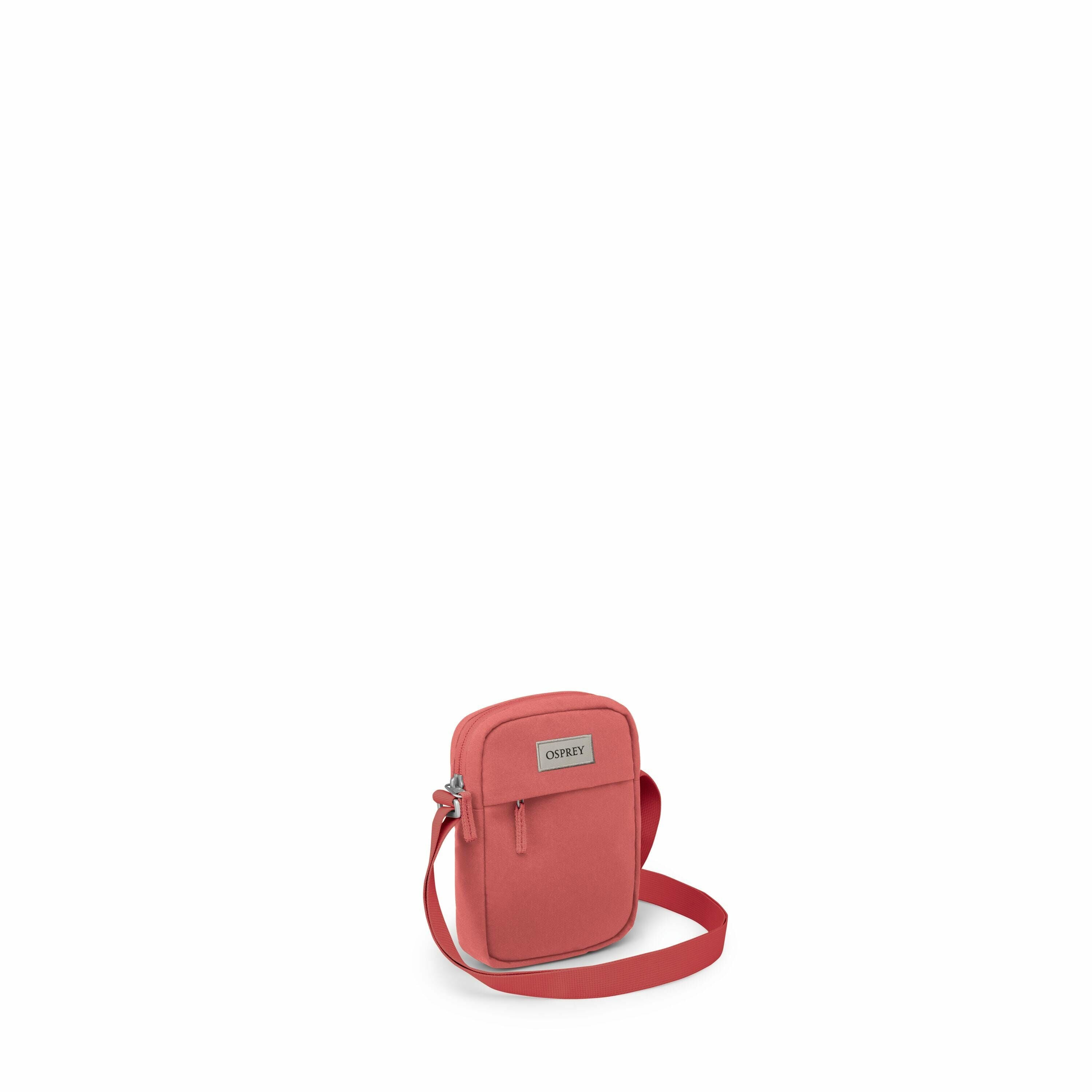 The image features a compact, coral-colored shoulder bag, likely designed for everyday use or travel. It is a small crossbody bag with a main compartment secured by a zipper, and it seems to have a front pocket also with a zip closure. The bag is accented