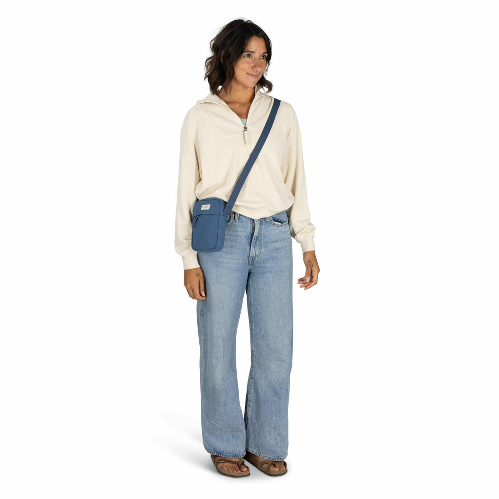 The image shows a person wearing casual attire. They are dressed in a cream-colored long-sleeve hoodie with a partial zipper at the collar, paired with light blue, high-waisted jeans with a wide-leg cut. They are carrying a small blue crossbody bag featur