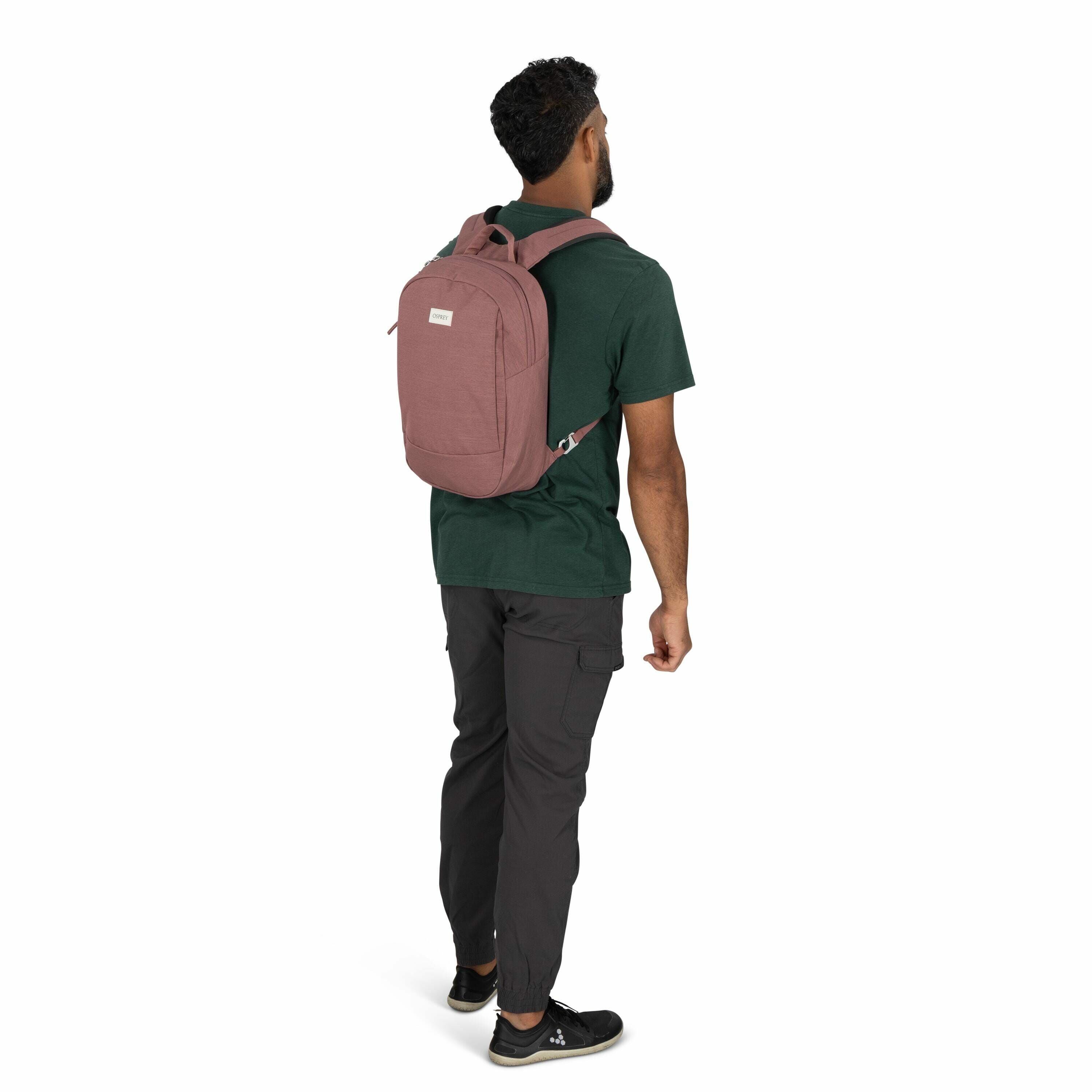 The image features a man standing with his back turned, wearing a casual outfit that includes a green t-shirt, dark grey cargo pants, and black sneakers. He has a burgundy backpack on his shoulders, which is secured with padded straps. The backpack has a