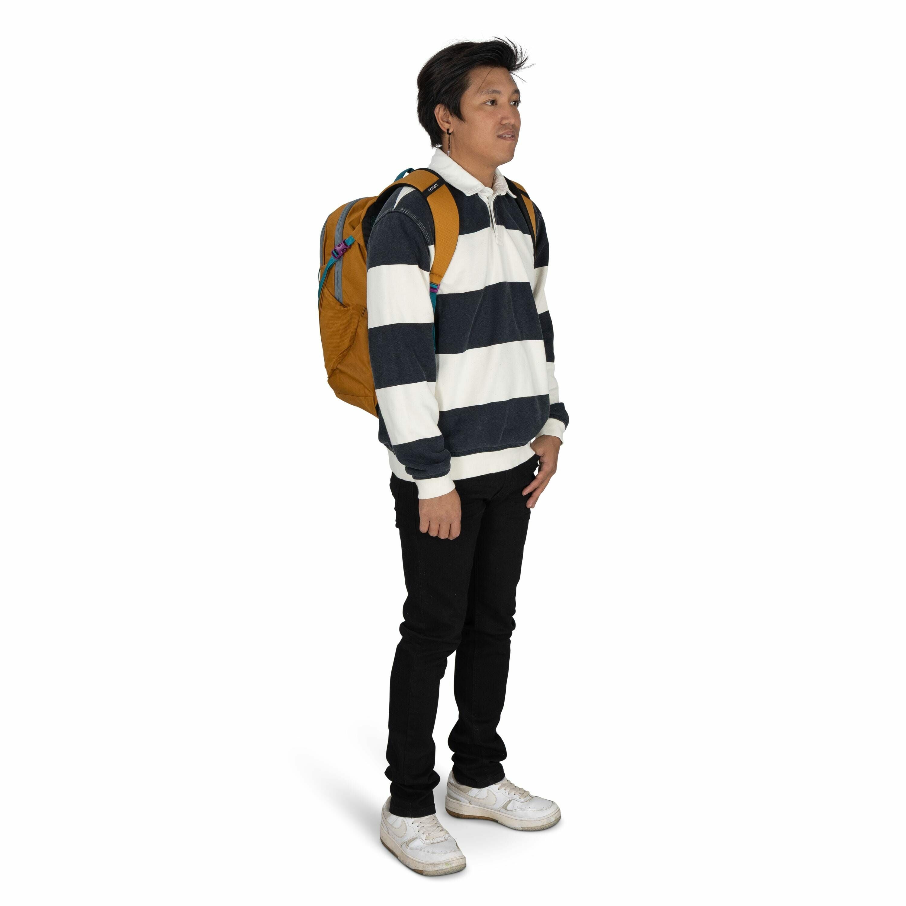 The image shows a person standing in a three-quarter view. They are wearing a black and white horizontally striped long-sleeve pullover with a collar, paired with black pants. On their back is a mustard-colored backpack with visible blue and purple straps
