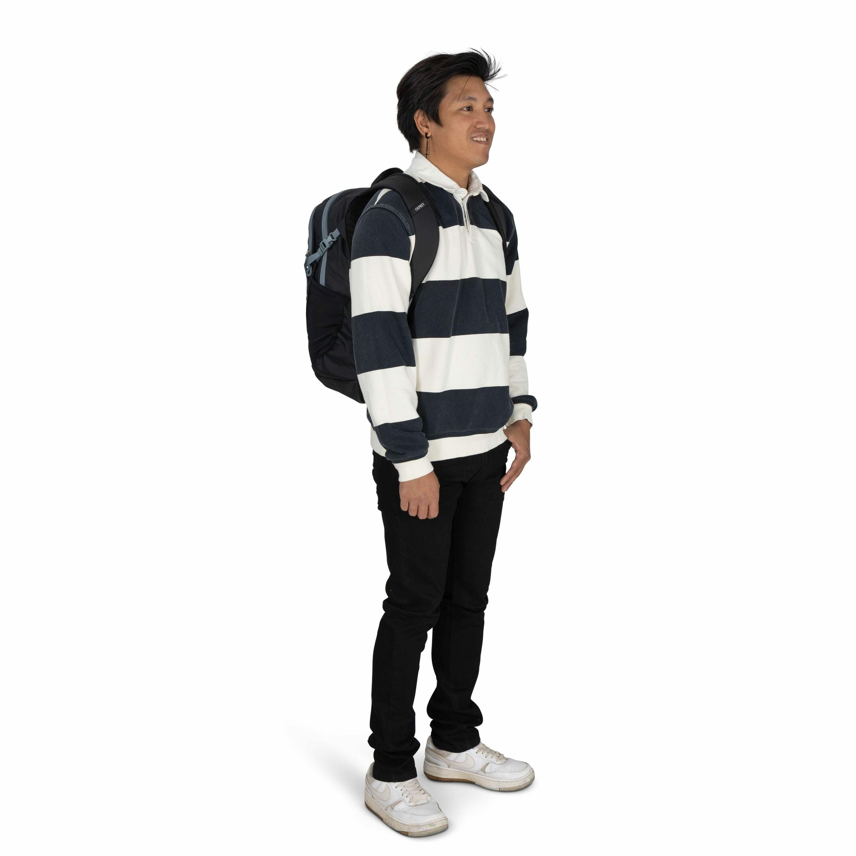 The image depicts a person standing and facing slightly to the left, carrying a dark-colored backpack on their back. The individual is wearing a long-sleeved rugby-style shirt with broad horizontal stripes in navy blue and white. They have paired this shi