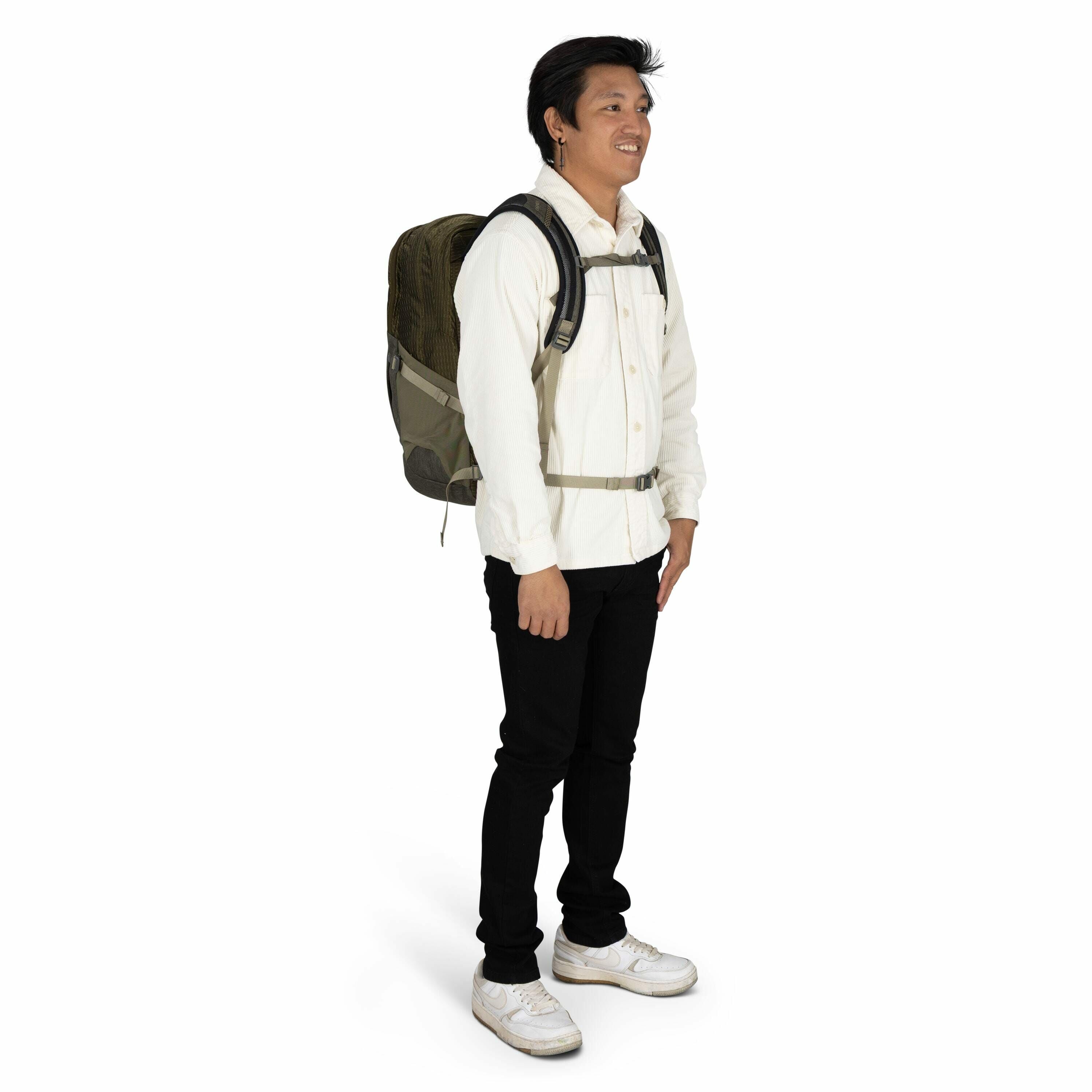 The image depicts a person standing and wearing a backpack. The individual is dressed in a white button-up shirt paired with black pants and white sneakers. The backpack appears to be dark green with a black strap and a chest buckle for support. The perso