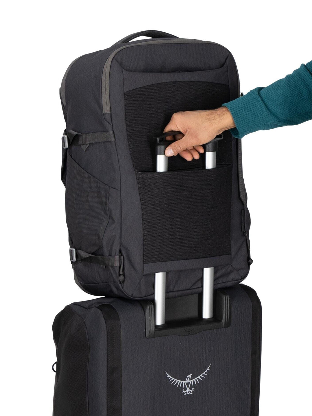 The image shows a person wearing a teal sweater, using a trolley luggage handle to hold an attachable backpack. The backpack is black and designed to slide over the trolley handle of a rolling suitcase, making it easy to transport together. The lower suit