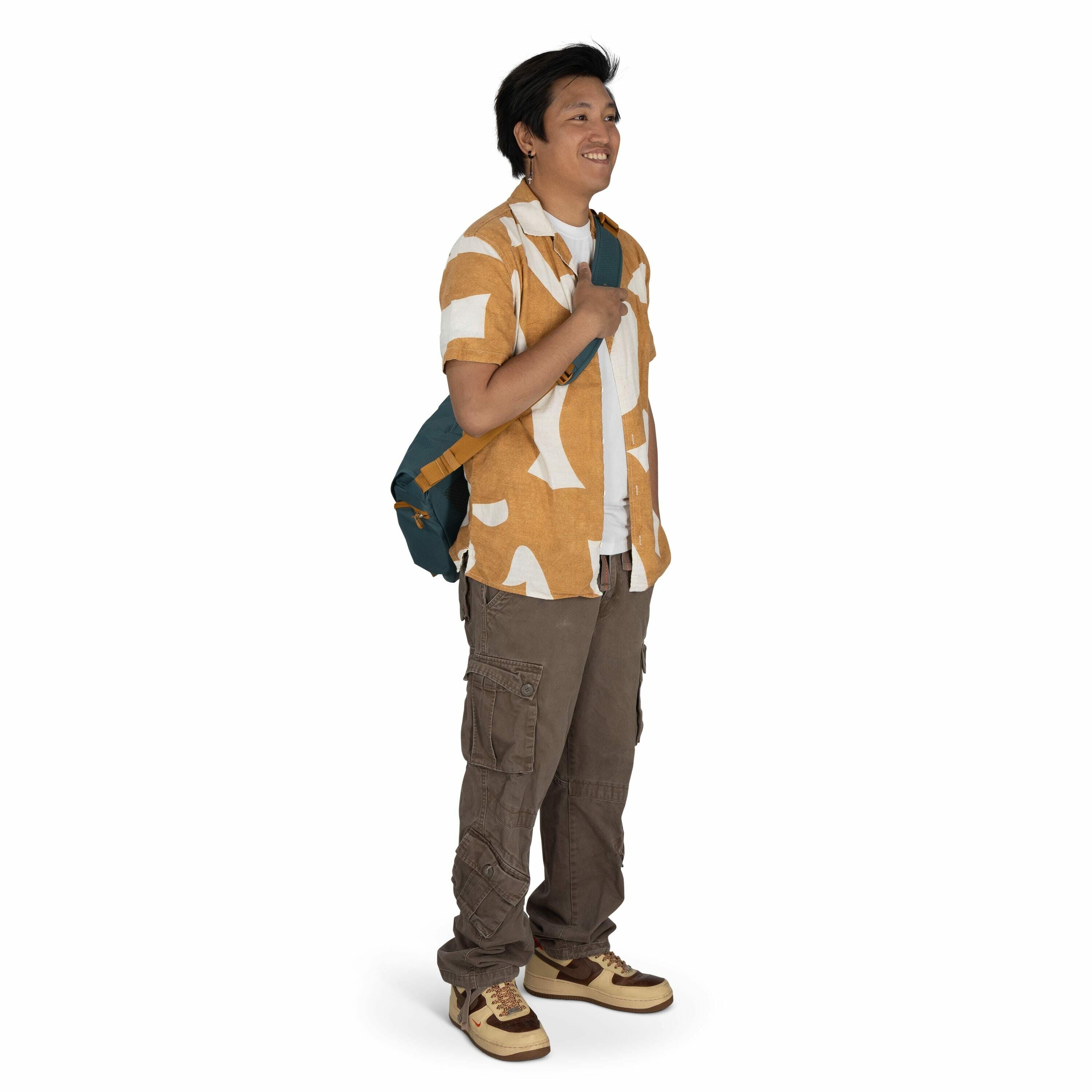 The image shows a person standing against a plain white background. They are wearing a short-sleeved shirt with a bold orange and white abstract pattern over a white T-shirt. They have brown cargo pants with multiple pockets and are wearing stylish sneake