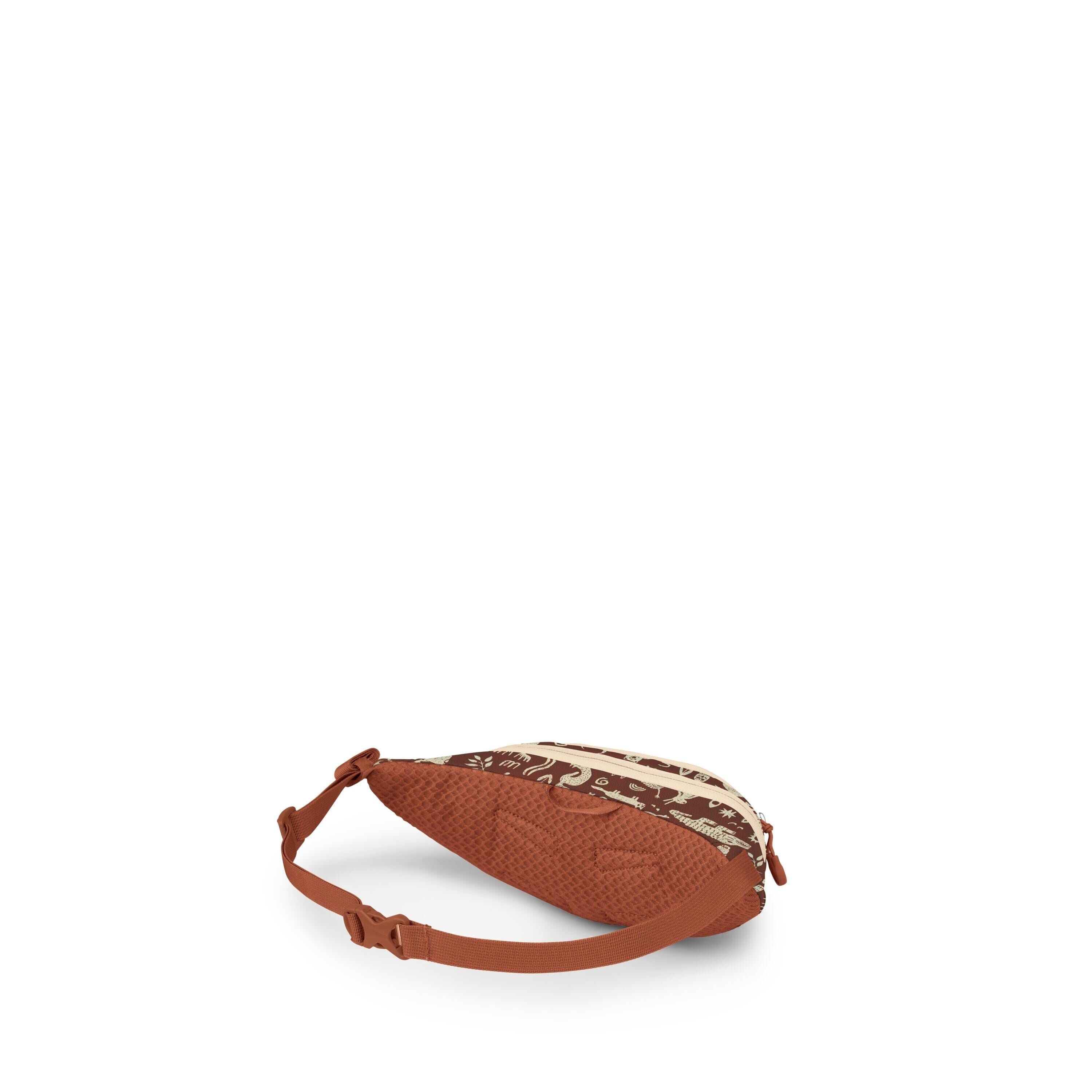 The images show a small waist bag or sling bag in a warm rust color with an adjustable strap and buckle. The top panel features a contrasting dark brown and cream pattern with animal and nature motifs, and there are two cream zippers along the top. The ba
