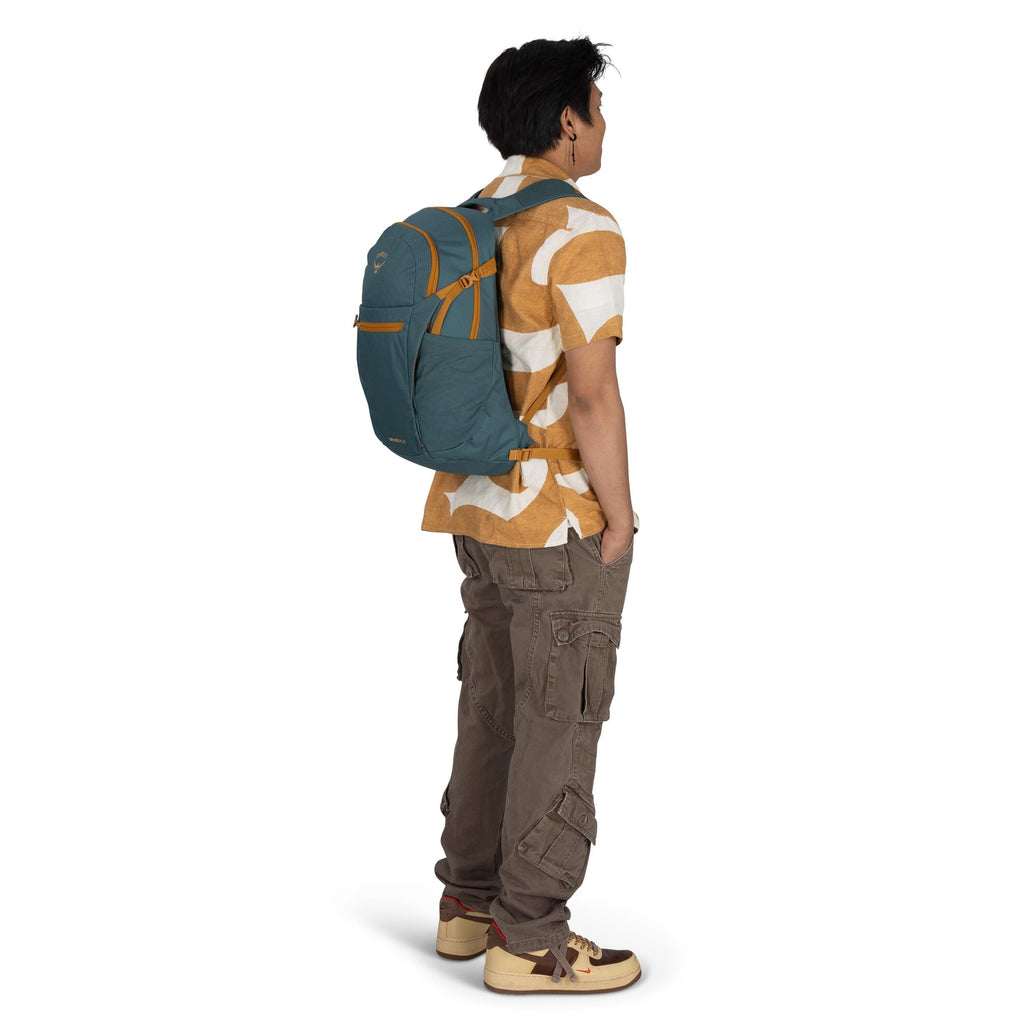 The image features a person standing in a side profile view. They are wearing a short-sleeved button-up shirt with a bold pattern in shades of brown and white, paired with brown cargo pants. On their feet are cream-colored sneakers with dark brown and red