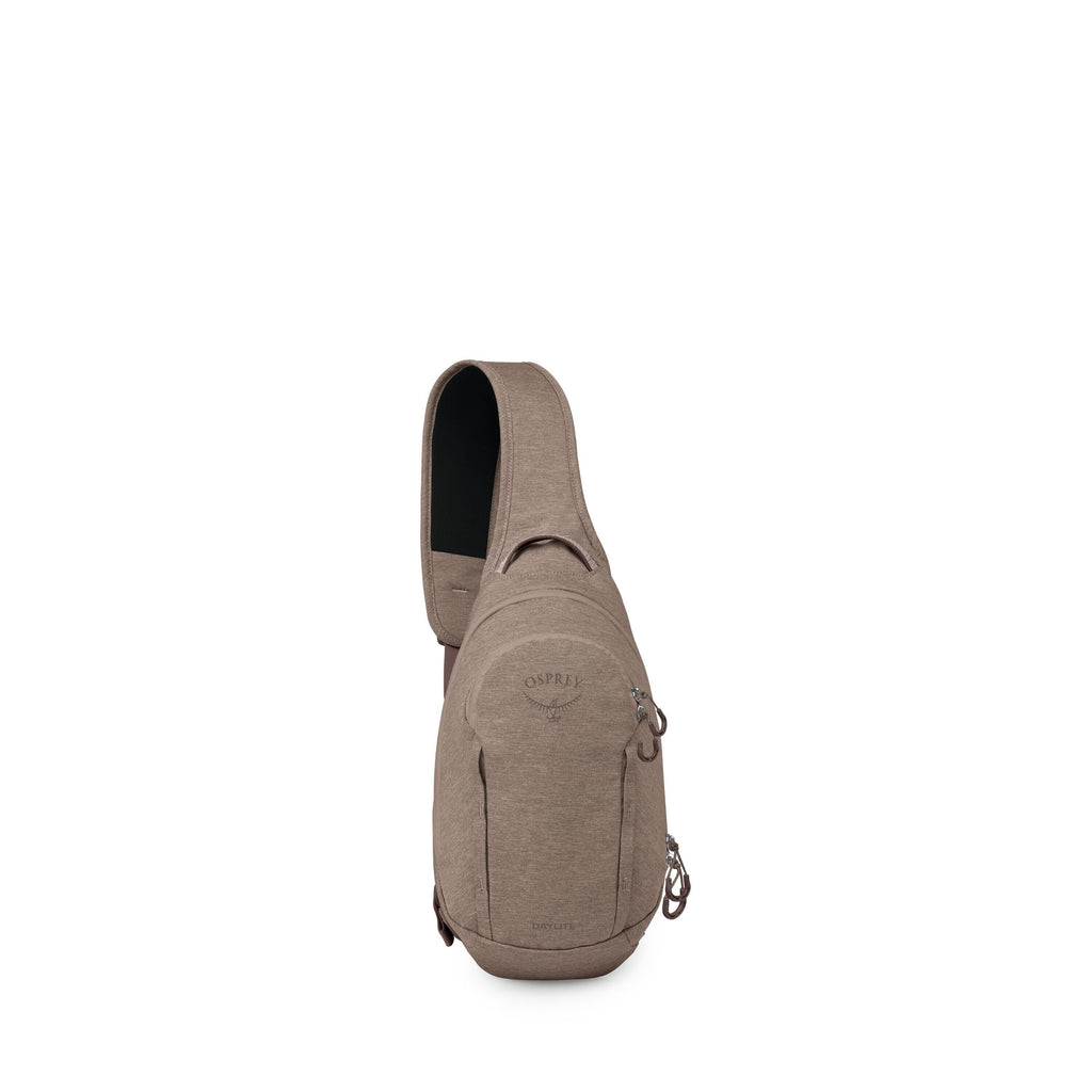 The image shows a compact, taupe-colored sling backpack standing upright against a white background. It has a single padded shoulder strap that crosses the body, a small top grab handle, and a rounded main compartment with a front zip pocket. The Osprey l