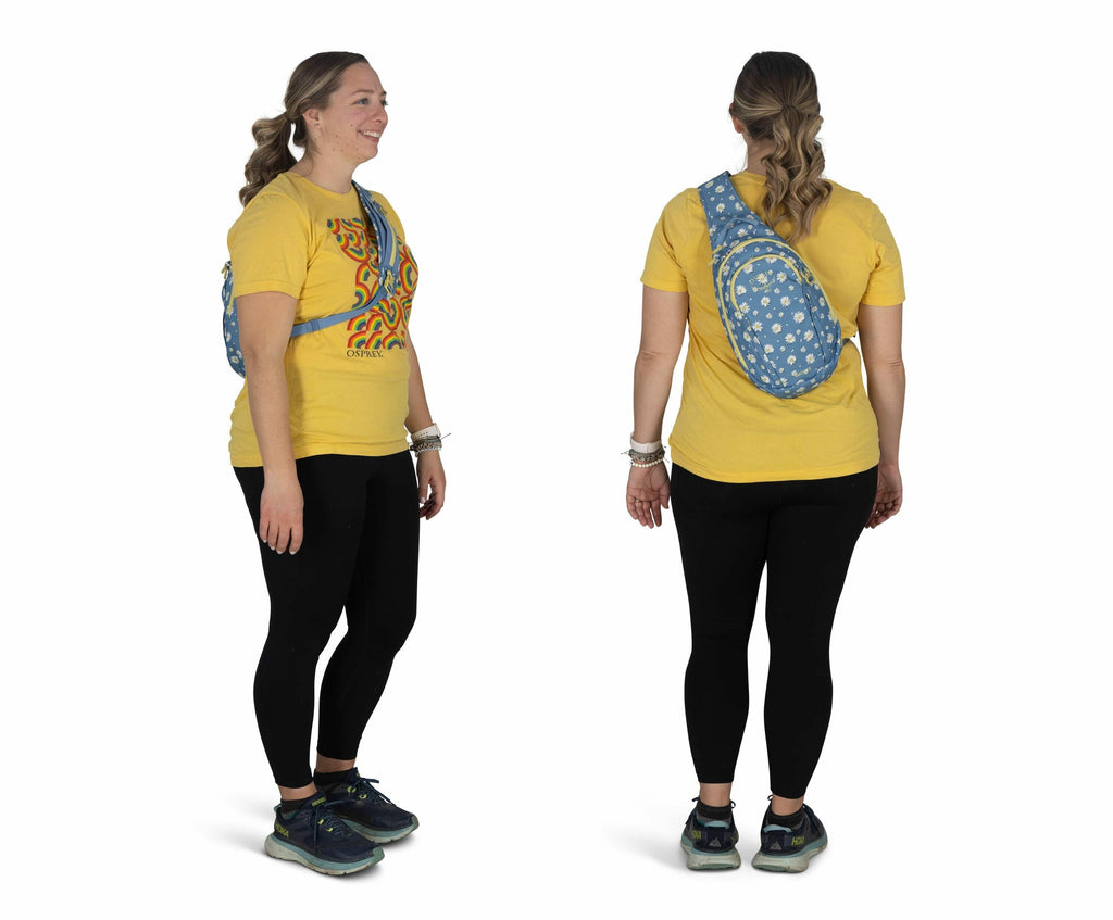 The image shows a person wearing a bright yellow t-shirt with a colorful abstract design on the front. The individual is also wearing black leggings and teal athletic shoes with turquoise details. They have a crossbody bag with a denim blue color featurin