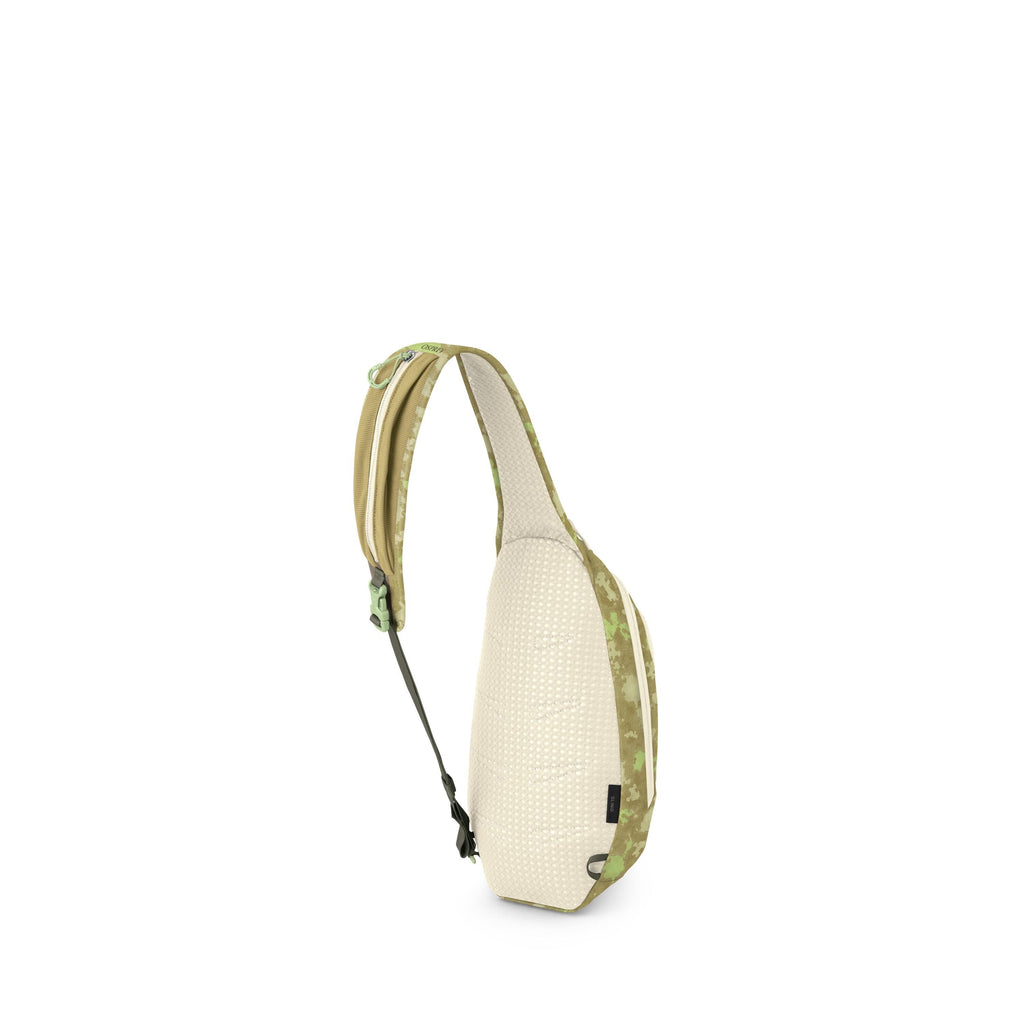 The image shows a small sling backpack in a light beige and green color scheme. It has a single padded strap with green camo accents and a buckle, designed to be worn crossbody. The back panel appears breathable with a dotted texture, and there's a zipper