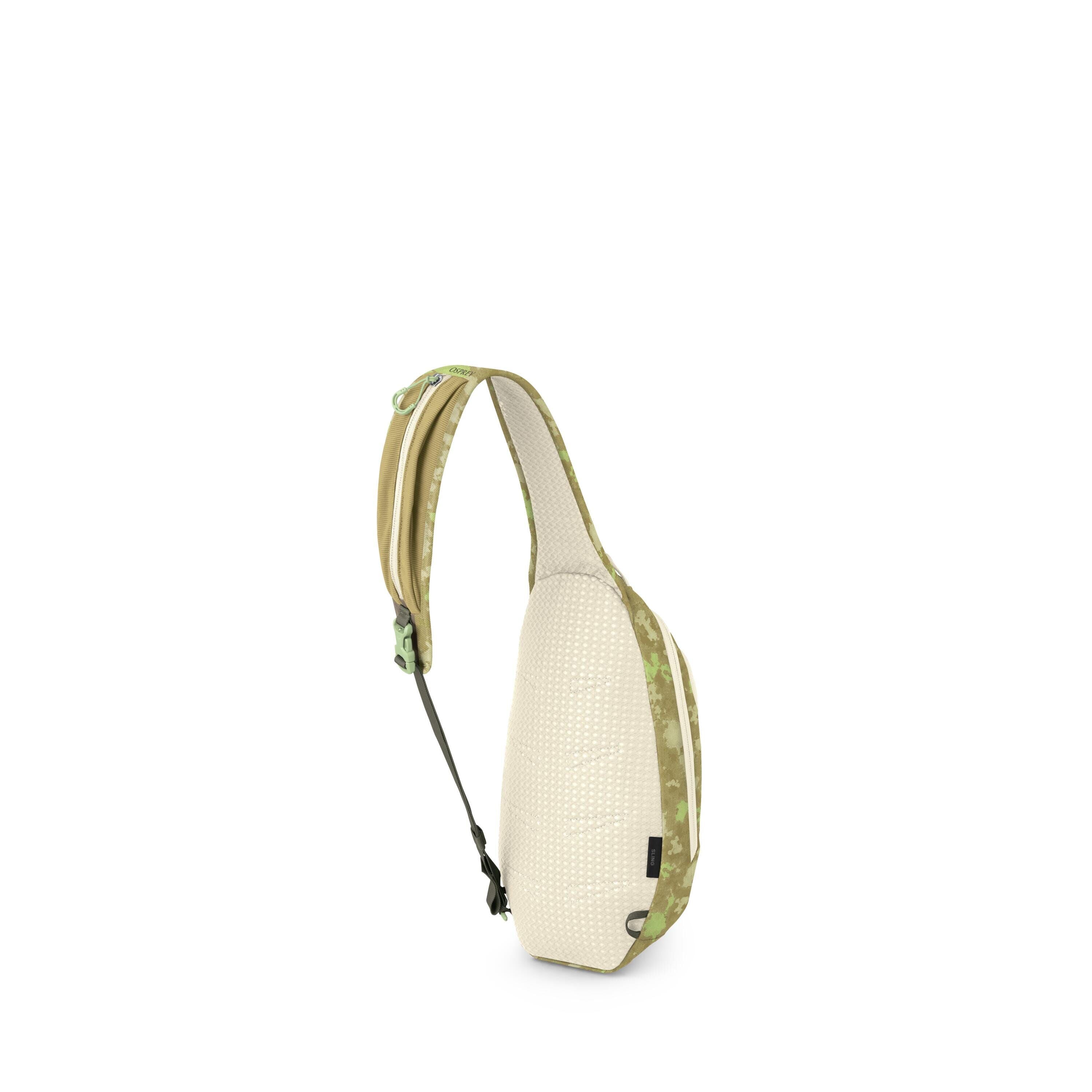 The image shows a small sling backpack in a light beige and green color scheme. It has a single padded strap with green camo accents and a buckle, designed to be worn crossbody. The back panel appears breathable with a dotted texture, and there's a zipper
