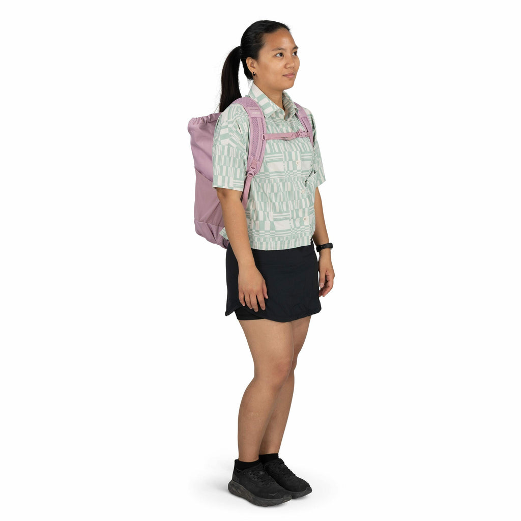 The image depicts a person standing in a side profile pose, wearing a patterned short-sleeved button-up shirt with a light green and white geometric design. They are also wearing a short black skirt and black athletic shoes paired with black socks. The pe