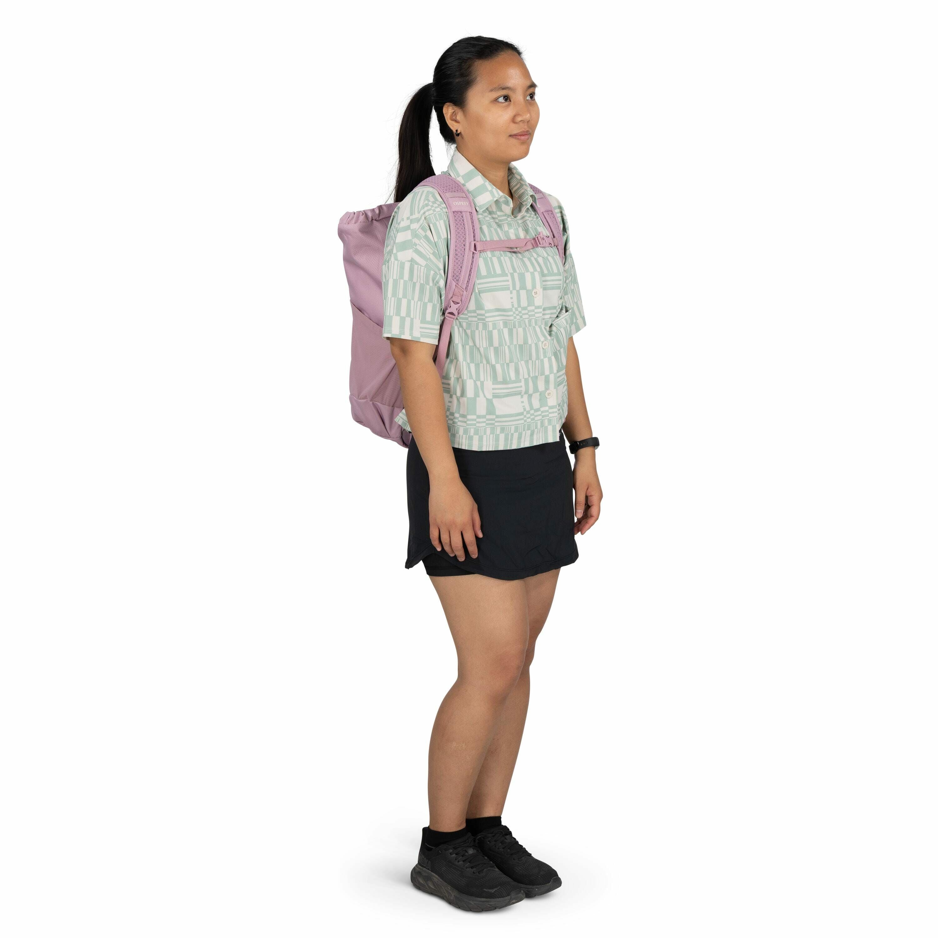 The image depicts a person standing in a side profile pose, wearing a patterned short-sleeved button-up shirt with a light green and white geometric design. They are also wearing a short black skirt and black athletic shoes paired with black socks. The pe