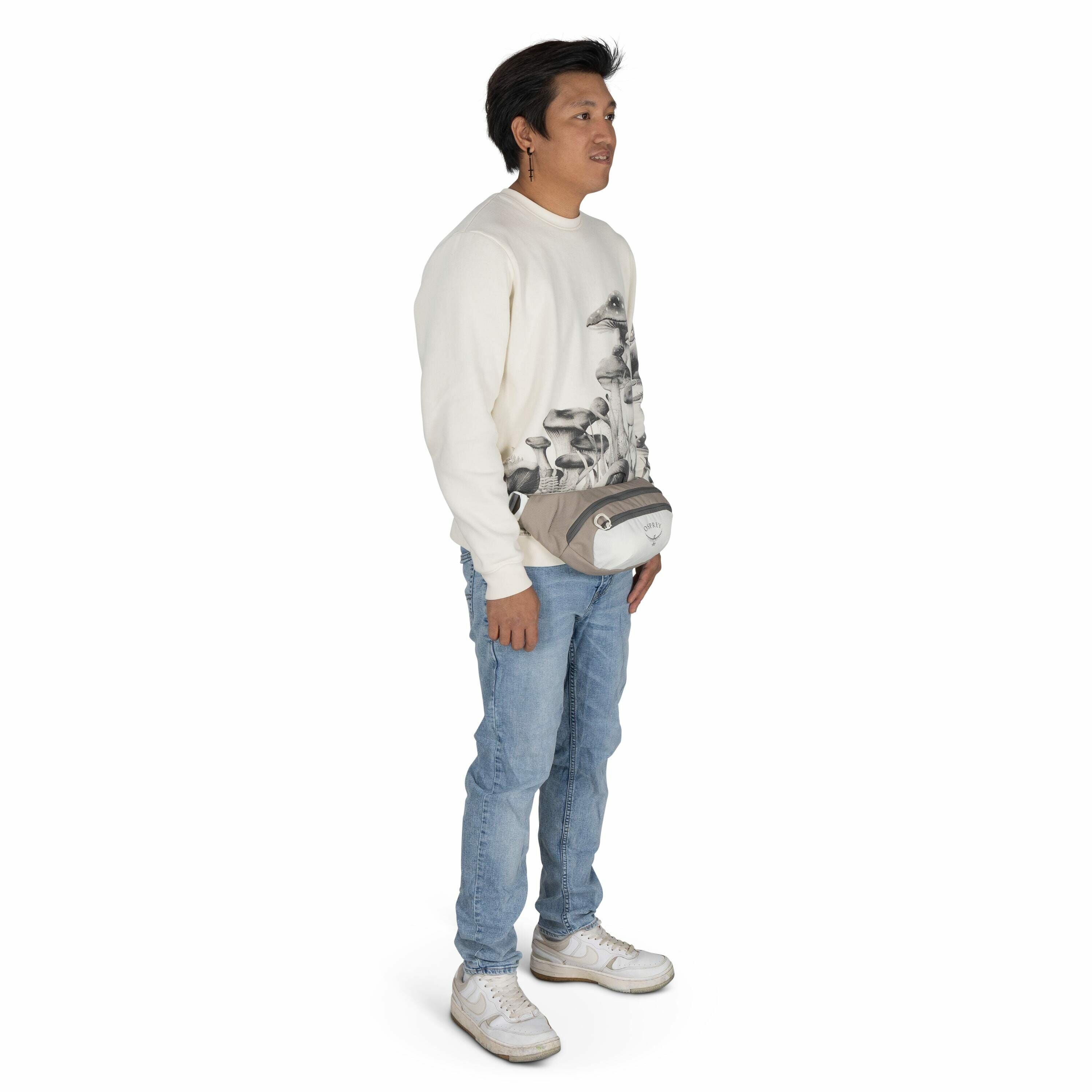 The image features a person standing, dressed casually. They are wearing a cream-colored sweatshirt adorned with a detailed mushroom pattern in grayscale towards the bottom. The individual is also wearing light blue jeans and white sneakers. Around their