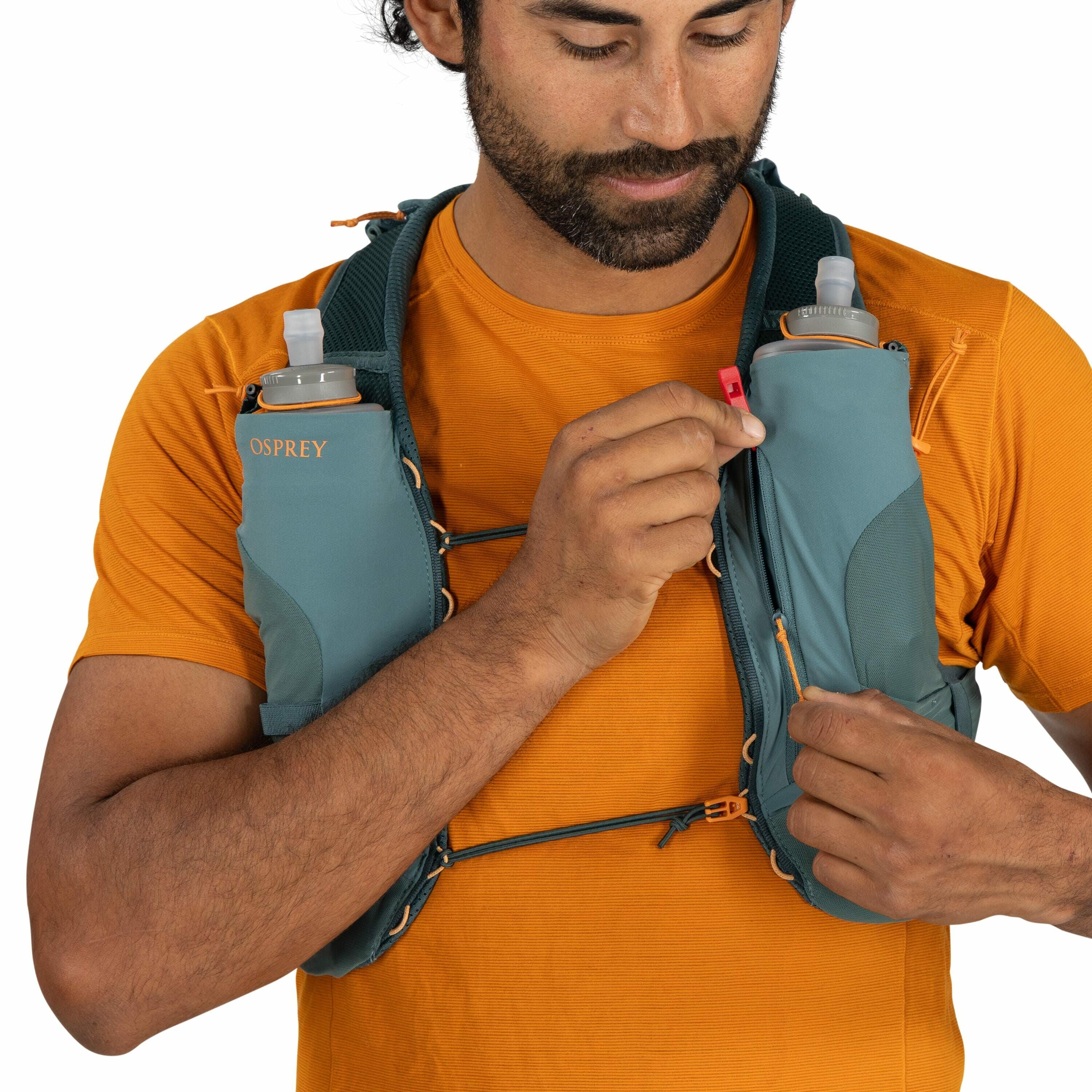 The image shows a person wearing an Osprey running or hydration vest. The vest is teal in color and features two pockets on the chest, each holding a clear water bottle with a nozzle for easy drinking. The person is wearing a bright orange T-shirt underne