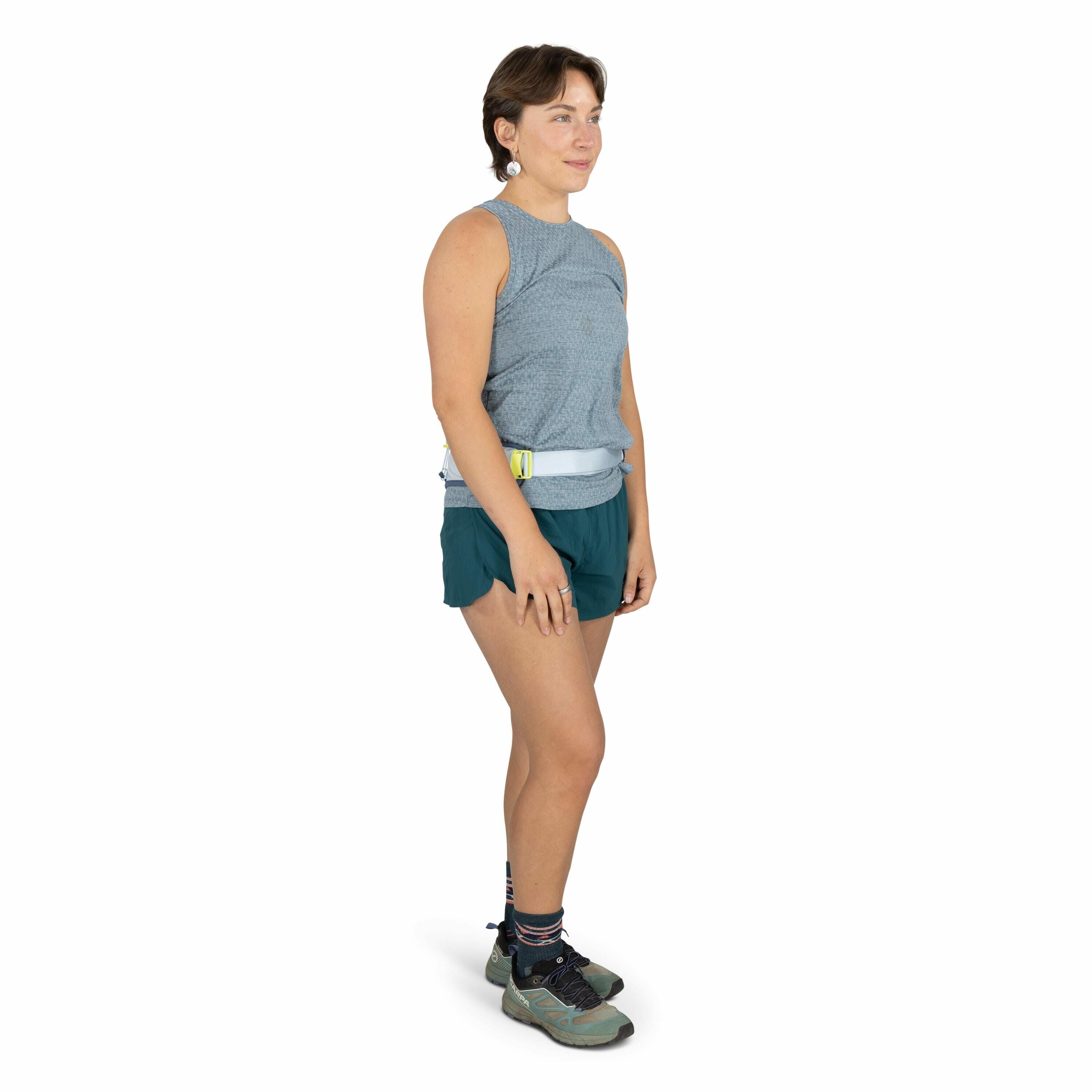 The image features a person standing in a relaxed pose, dressed in activewear suitable for outdoor activities or sports. They are wearing a sleeveless, light blue patterned top paired with teal shorts and a belt bag around the waist, which could be used f