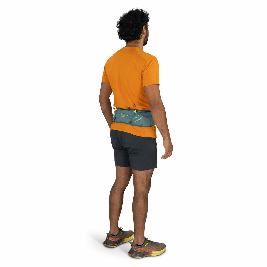The image features a man facing away from the camera, showcasing the back view of his outfit. He is dressed in a bright orange short-sleeve shirt paired with dark gray shorts. Around his waist, he is wearing a blue waist pack with lime green accents and t
