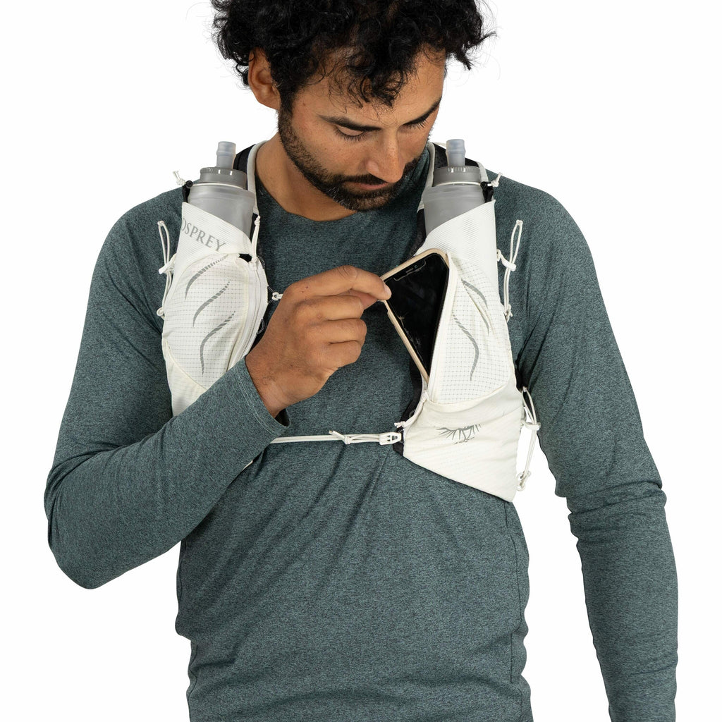 The image depicts a person wearing a teal-colored long-sleeved shirt and an Osprey hydration vest. The vest has two visible pockets on the chest area, each holding a hydration bottle labeled "Osprey." The person is holding a smartphone, partially inserted
