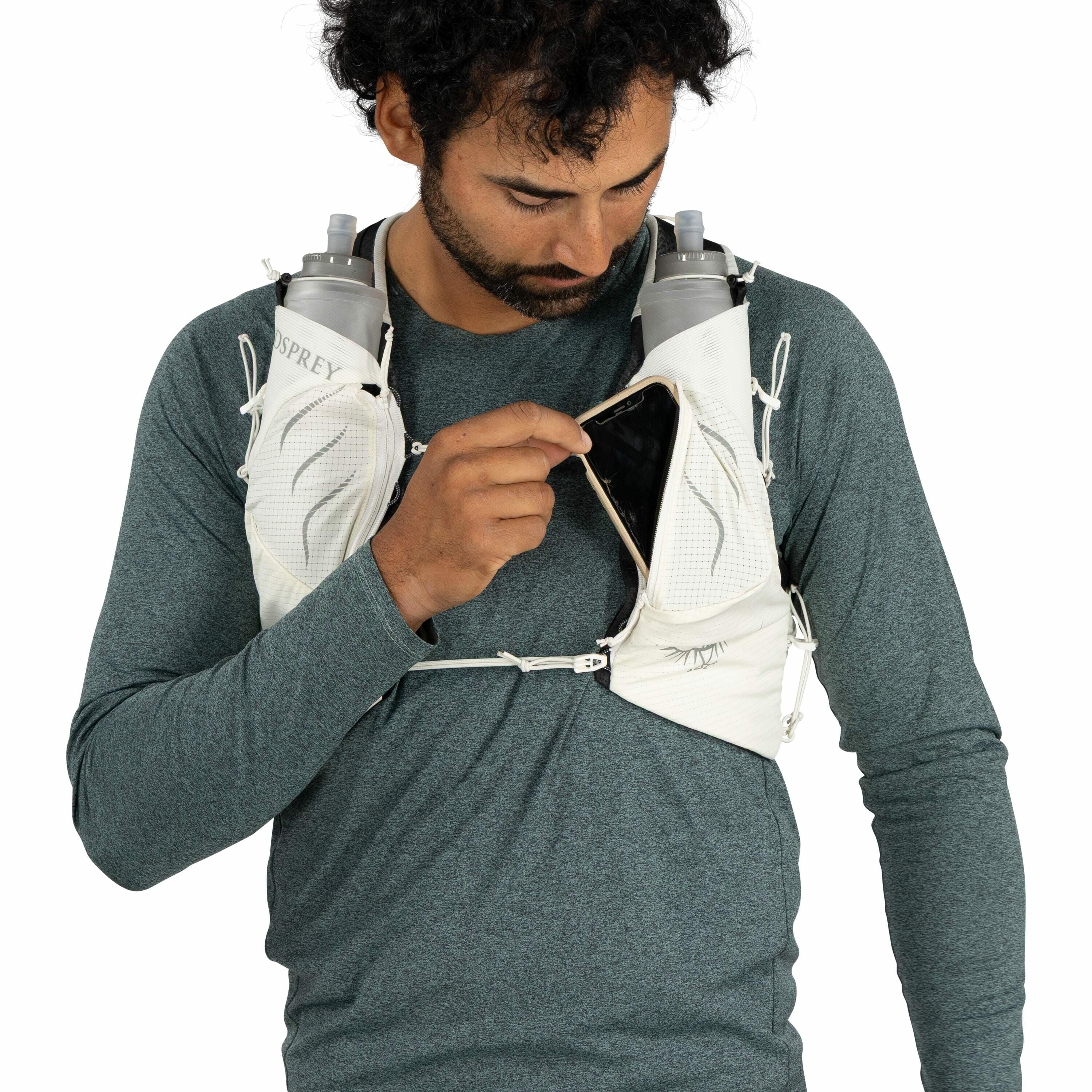 The image depicts a person wearing a teal-colored long-sleeved shirt and an Osprey hydration vest. The vest has two visible pockets on the chest area, each holding a hydration bottle labeled "Osprey." The person is holding a smartphone, partially inserted