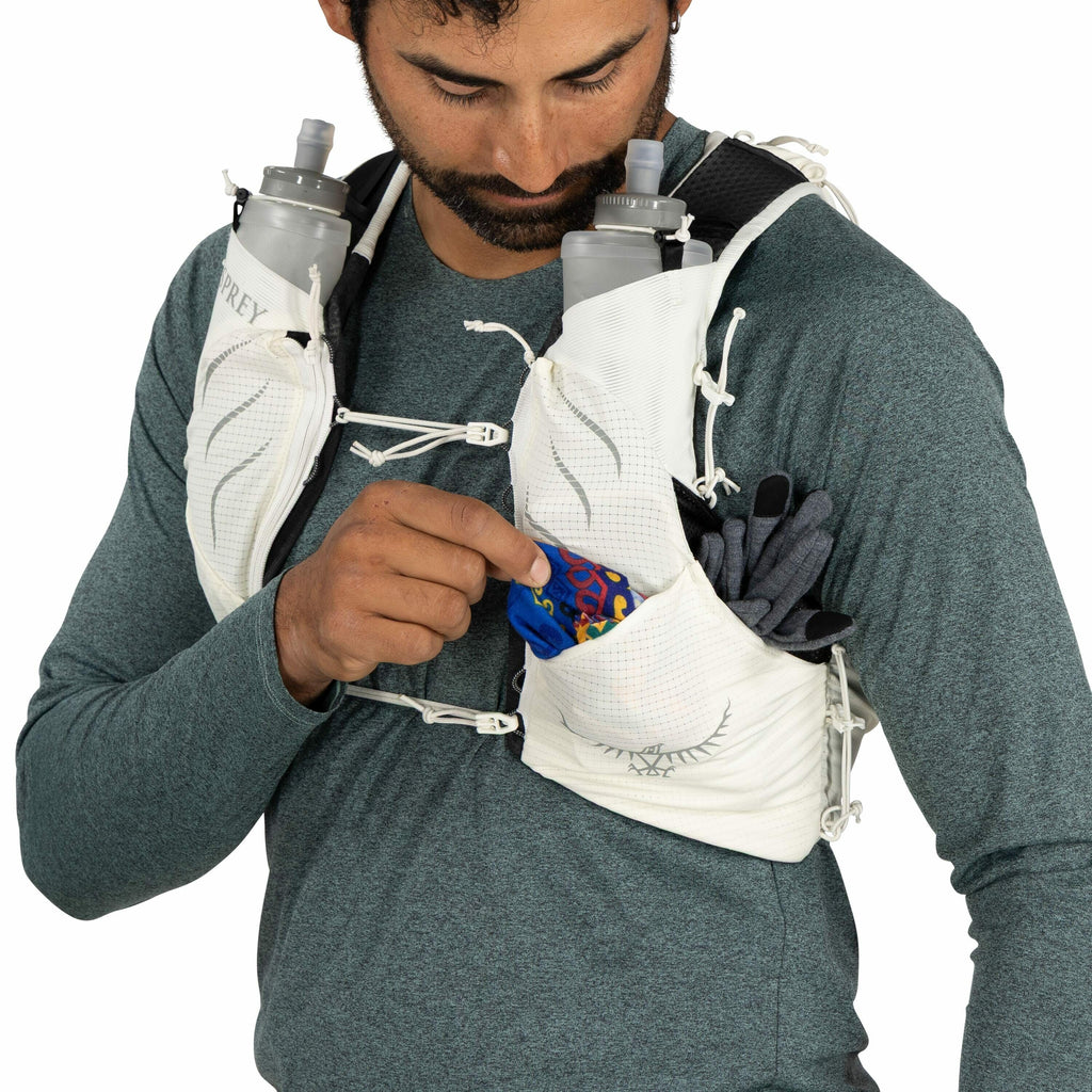 The image shows a person wearing a running hydration vest, which appears to be made by Osprey, as indicated by the logo on the vest. The vest is white with black accents and features multiple pockets designed for storing gear and essentials while running.