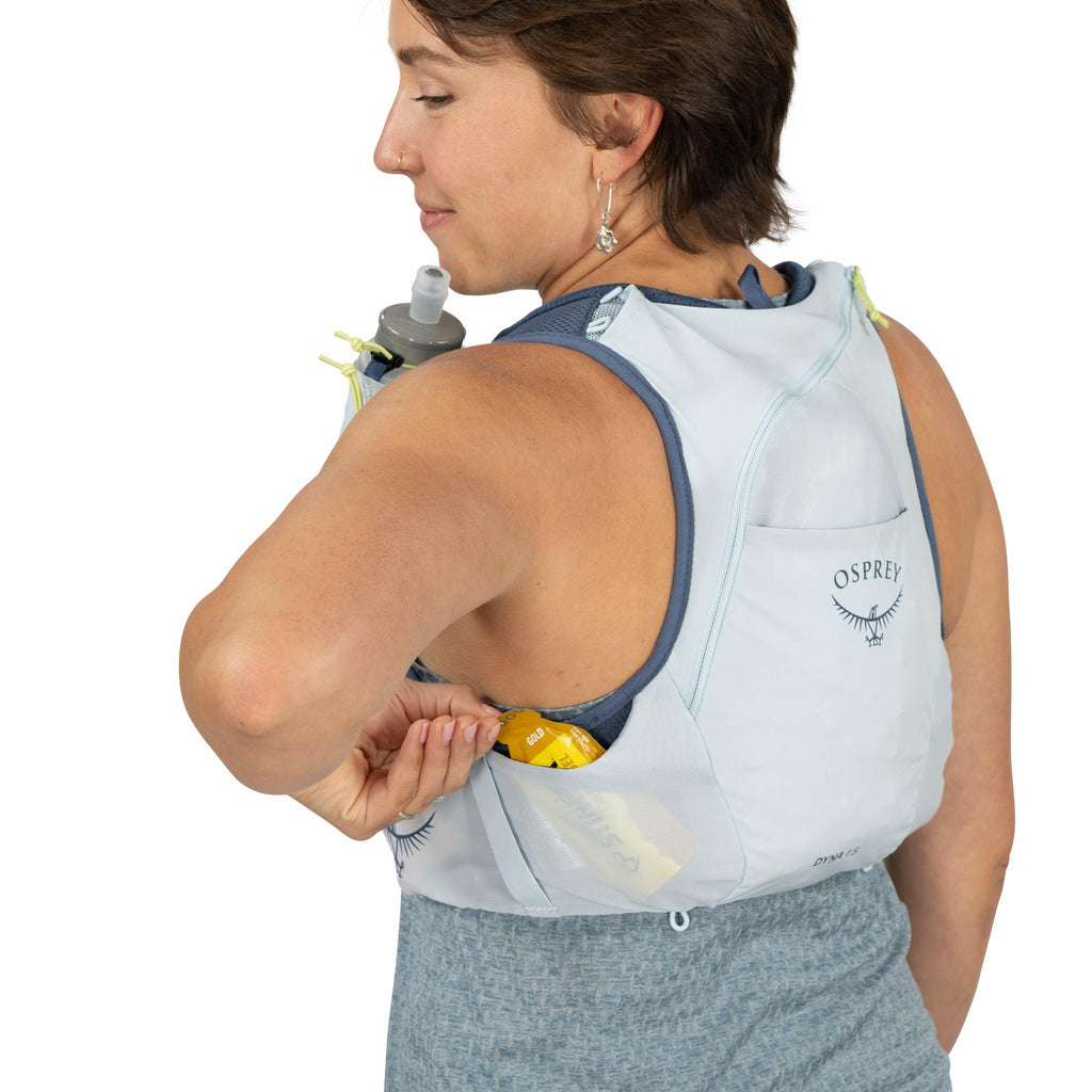 The image shows a person wearing a light gray Osprey running hydration vest. The vest is designed for athletes, with a pocket containing energy gels for easy access. The person is adjusting or reaching into the pocket located under their arm. The vest has