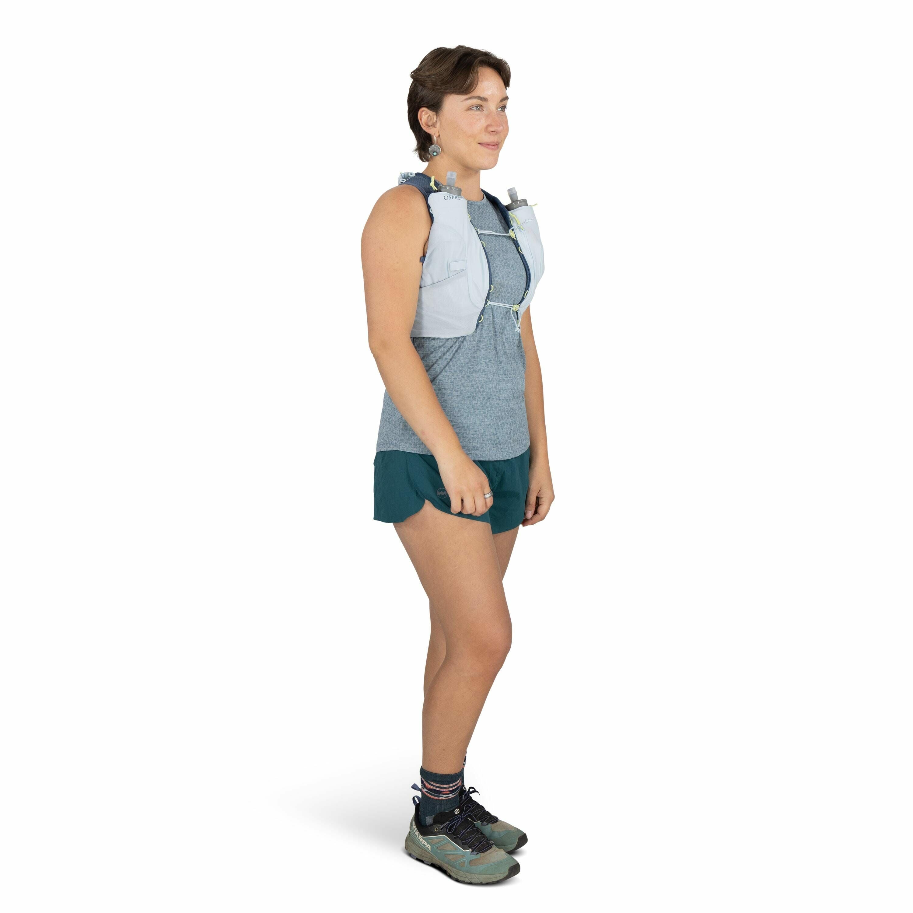 The image features a person standing in a side profile pose, dressed in athletic attire suitable for running or hiking. The individual is wearing a grey and white running vest with the CamelBak logo visible, which suggests it's likely equipped for carryin