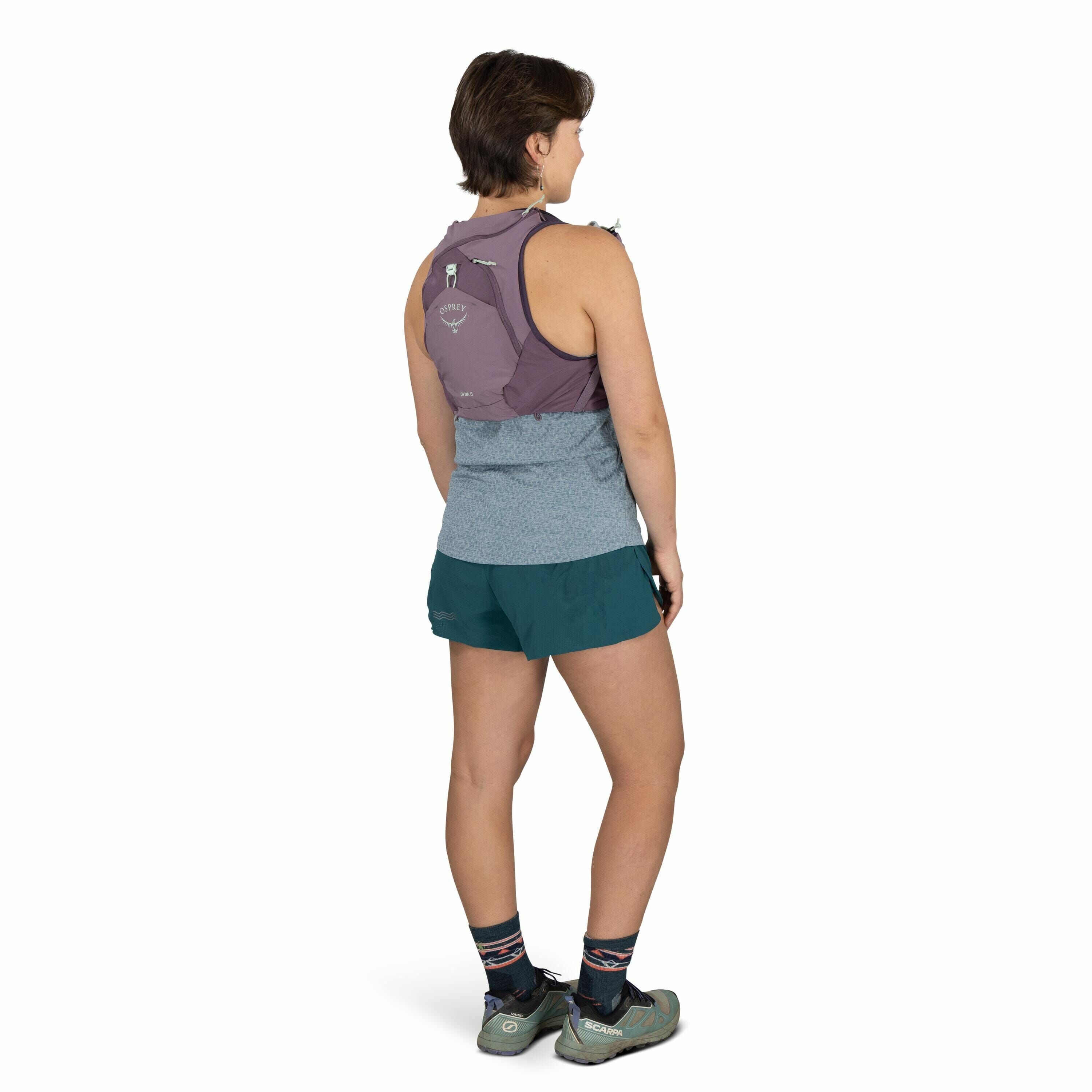 The image shows a person standing and facing away from the camera, dressed in athletic wear suitable for outdoor activities or running. They are wearing a sleeveless gray top and teal shorts, along with a purple Osprey backpack that features the brand's l