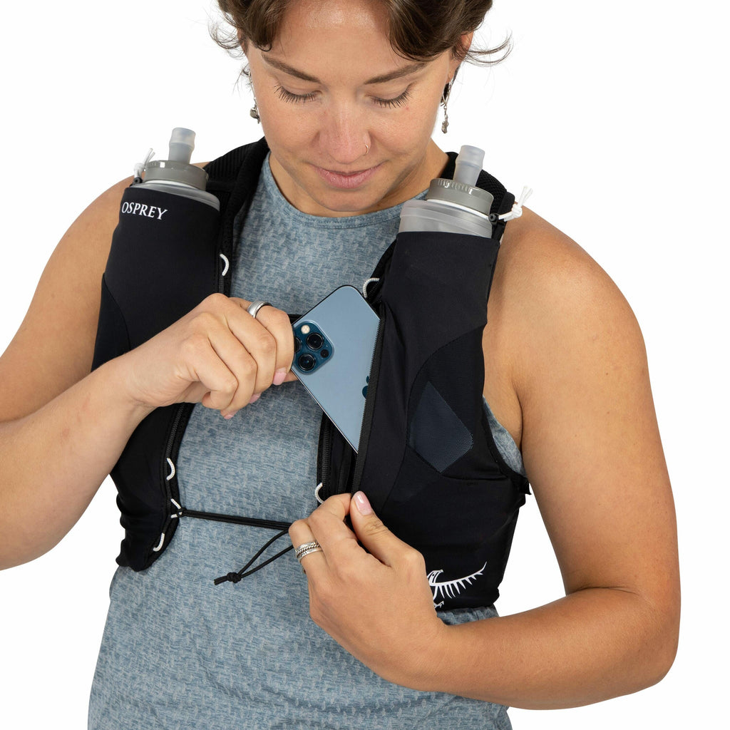 The image shows a person wearing a black hydration vest with two water bottles placed in front pockets on either side of the vest. The vest has the brand name "Osprey" visible near the shoulder area. The individual is holding a smartphone, which appears t