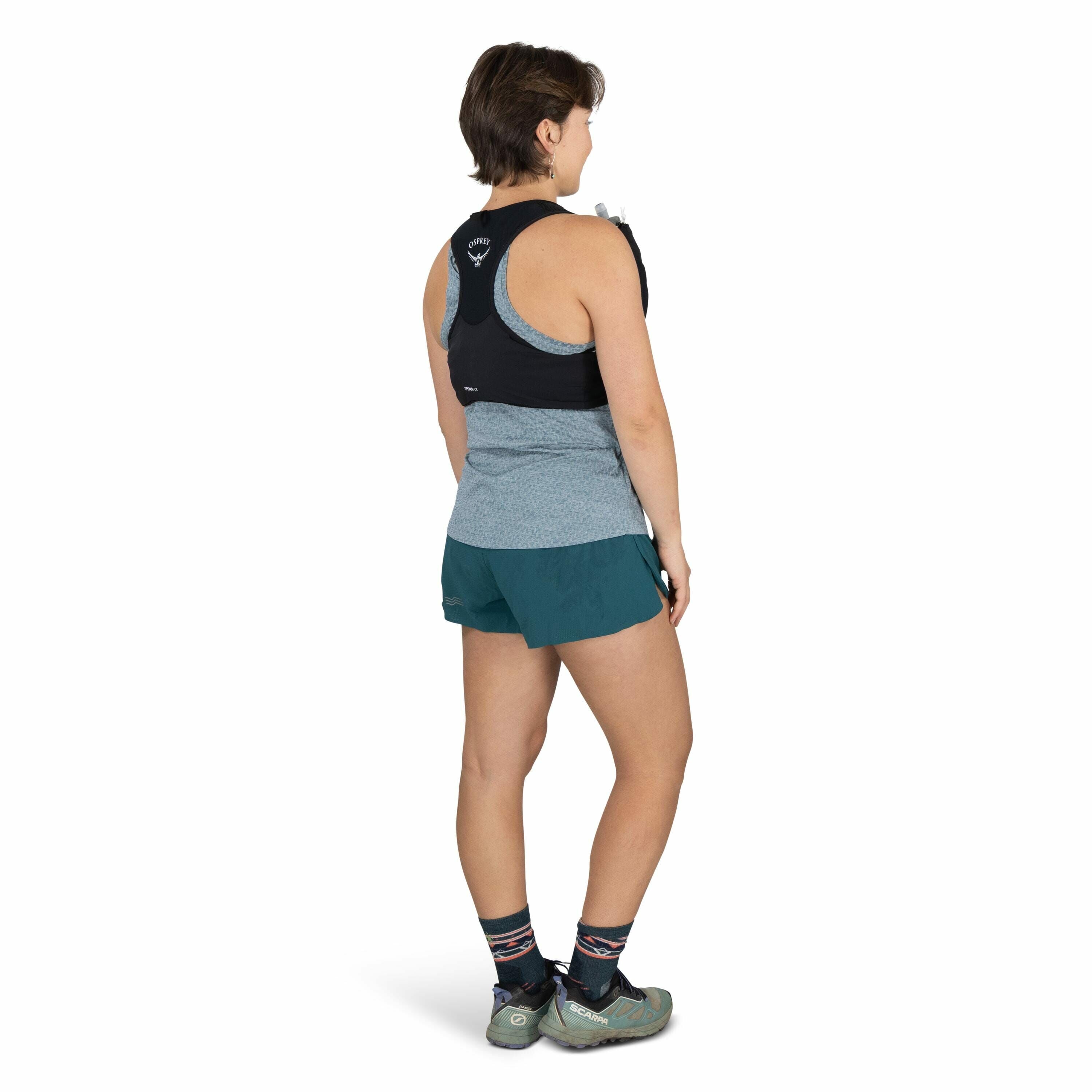 The image features a person standing and facing away from the camera. They are wearing a black and grey athletic tank top, teal shorts, and athletic shoes. Additionally, they have a small black hydration pack on their back, visible with an Osprey logo on