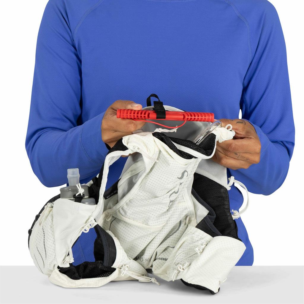 The image shows a person wearing a bright blue long-sleeve shirt, focused on holding a hydration vest and a red hydration bladder reservoir. The hydration vest is white and appears to be made of a breathable, lightweight material, with pockets and compart