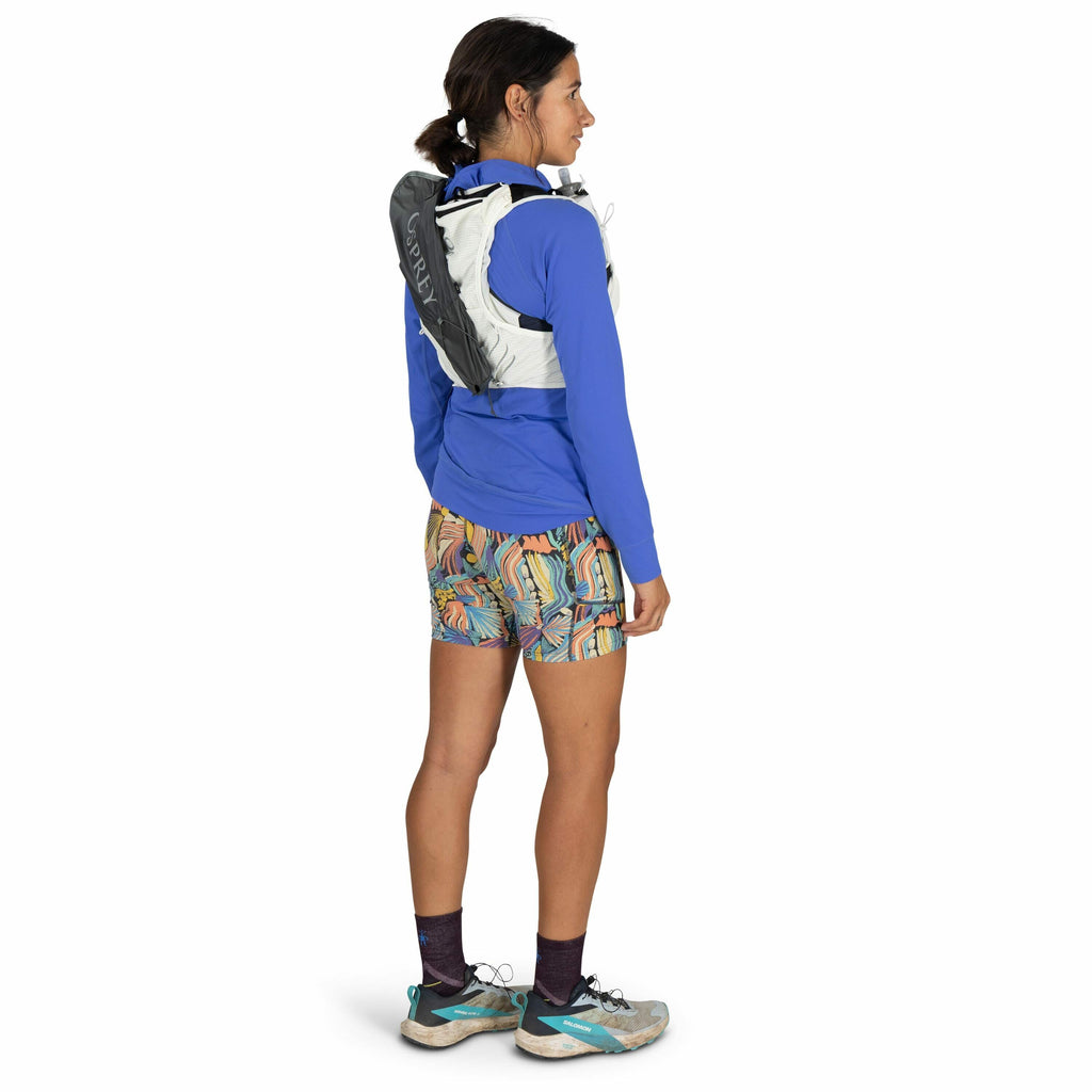 The image depicts a person dressed in athletic attire, viewed from the side and slightly from the back. The individual is wearing a bright blue long-sleeve top and colorful shorts with a vibrant, abstract pattern featuring curved lines and shapes. They ha