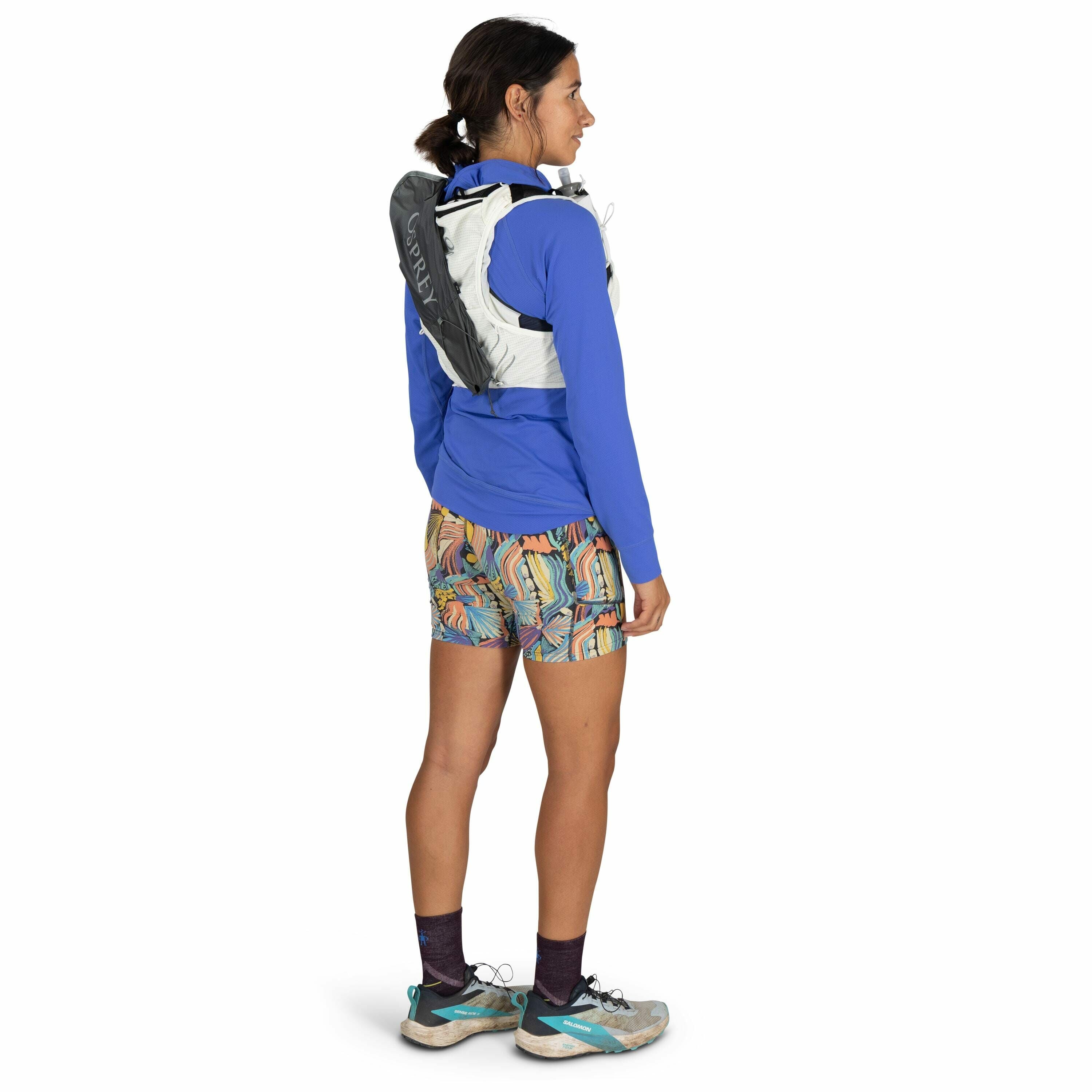 The image depicts a person dressed in athletic attire, viewed from the side and slightly from the back. The individual is wearing a bright blue long-sleeve top and colorful shorts with a vibrant, abstract pattern featuring curved lines and shapes. They ha